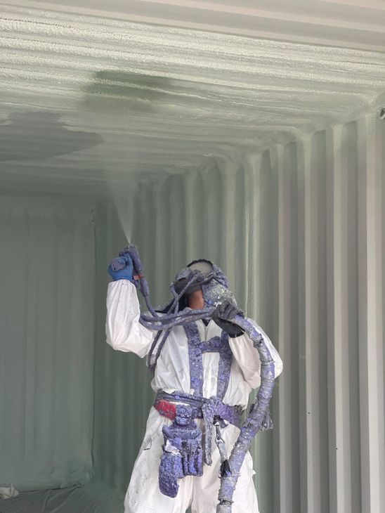 A man is spraying foam on the ceiling of a shipping container.