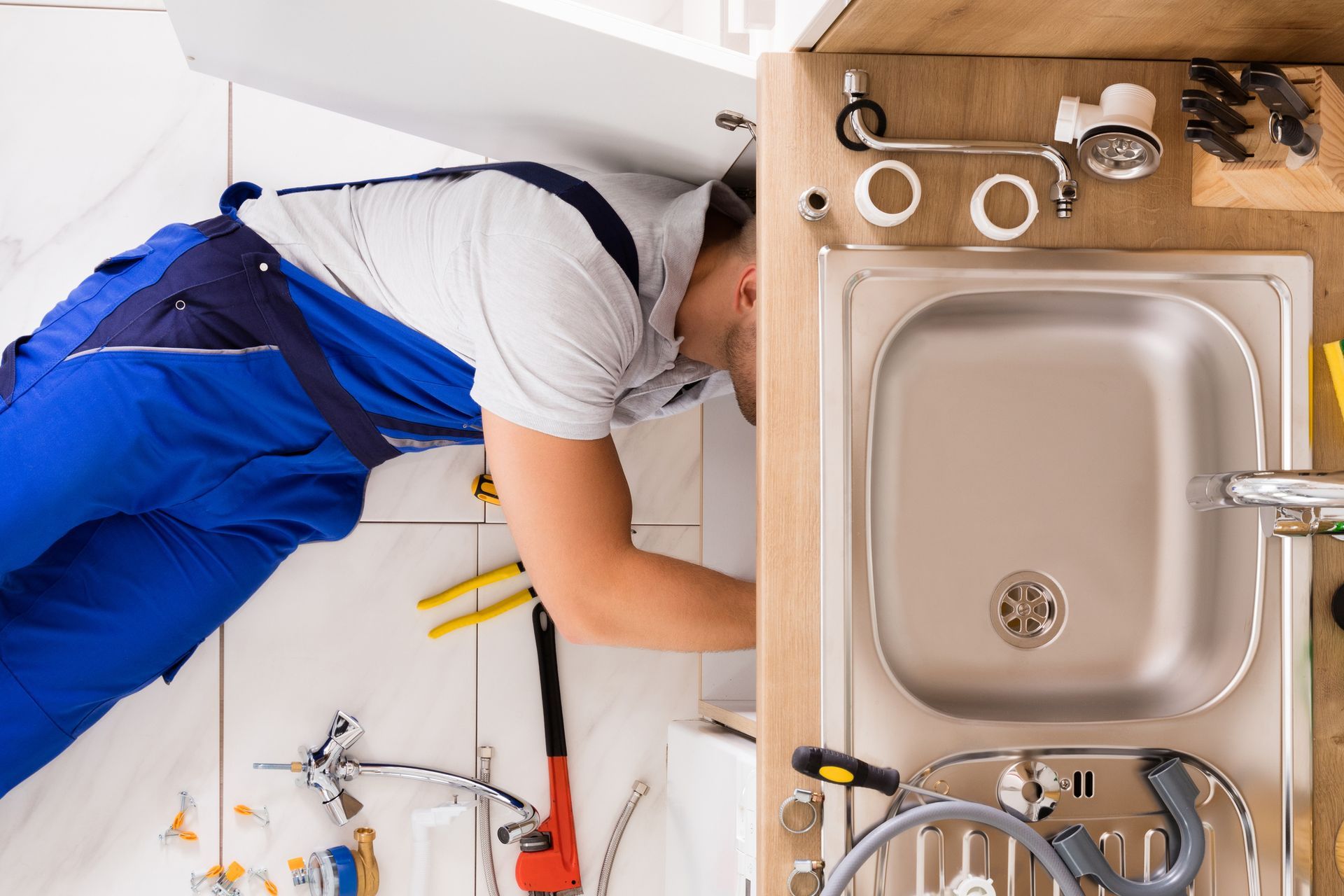 Plumber in uniform working under sink pipe, viewed from above. Plumber in uniform working under sink pipe, viewed from above.