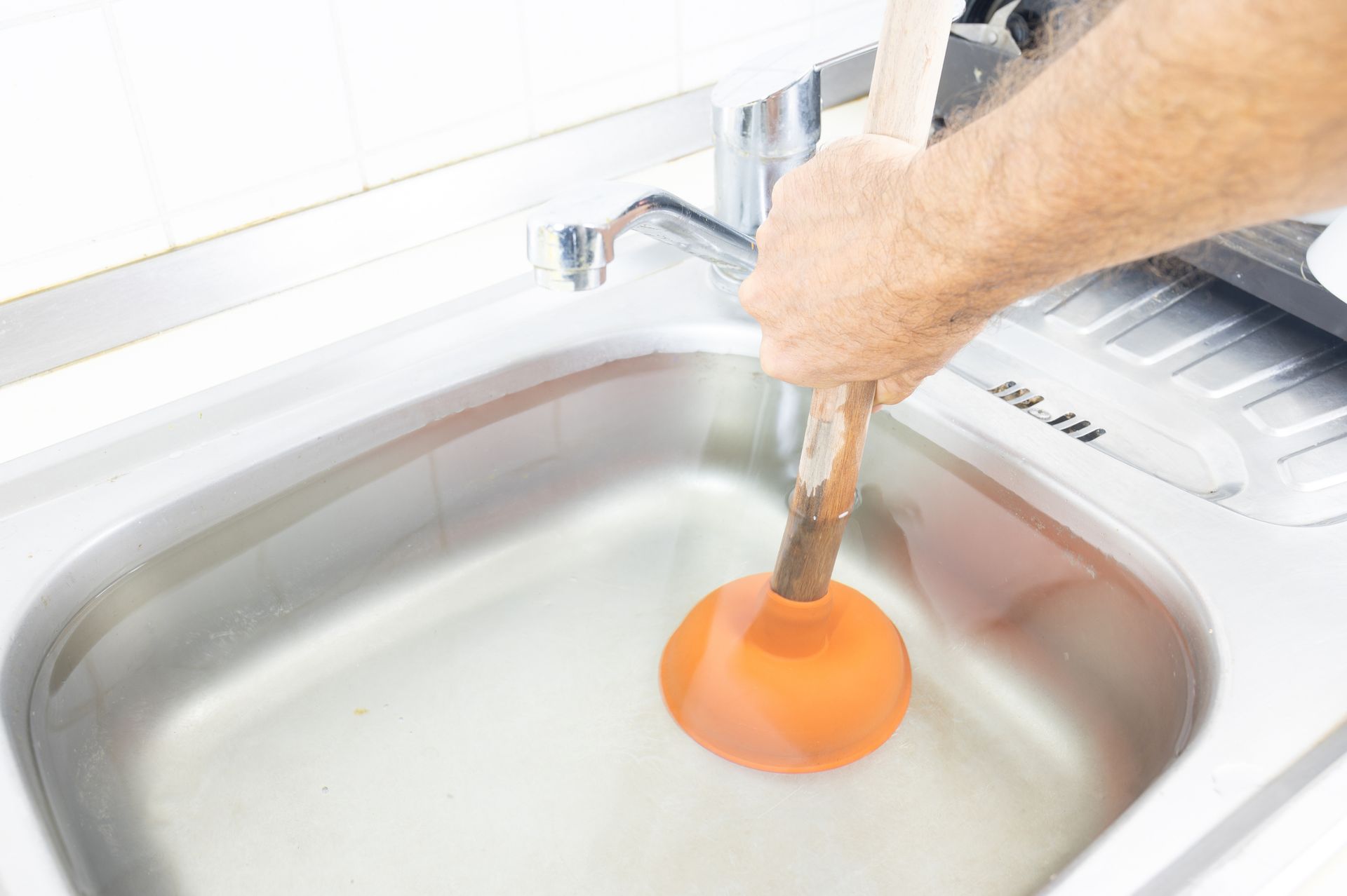 A person uses a plunger to unclog a kitchen sink filled with water, demonstrating plumbing repair.