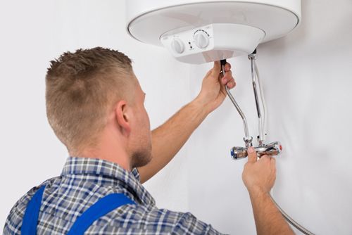 A man is fixing a water heater on a wall.