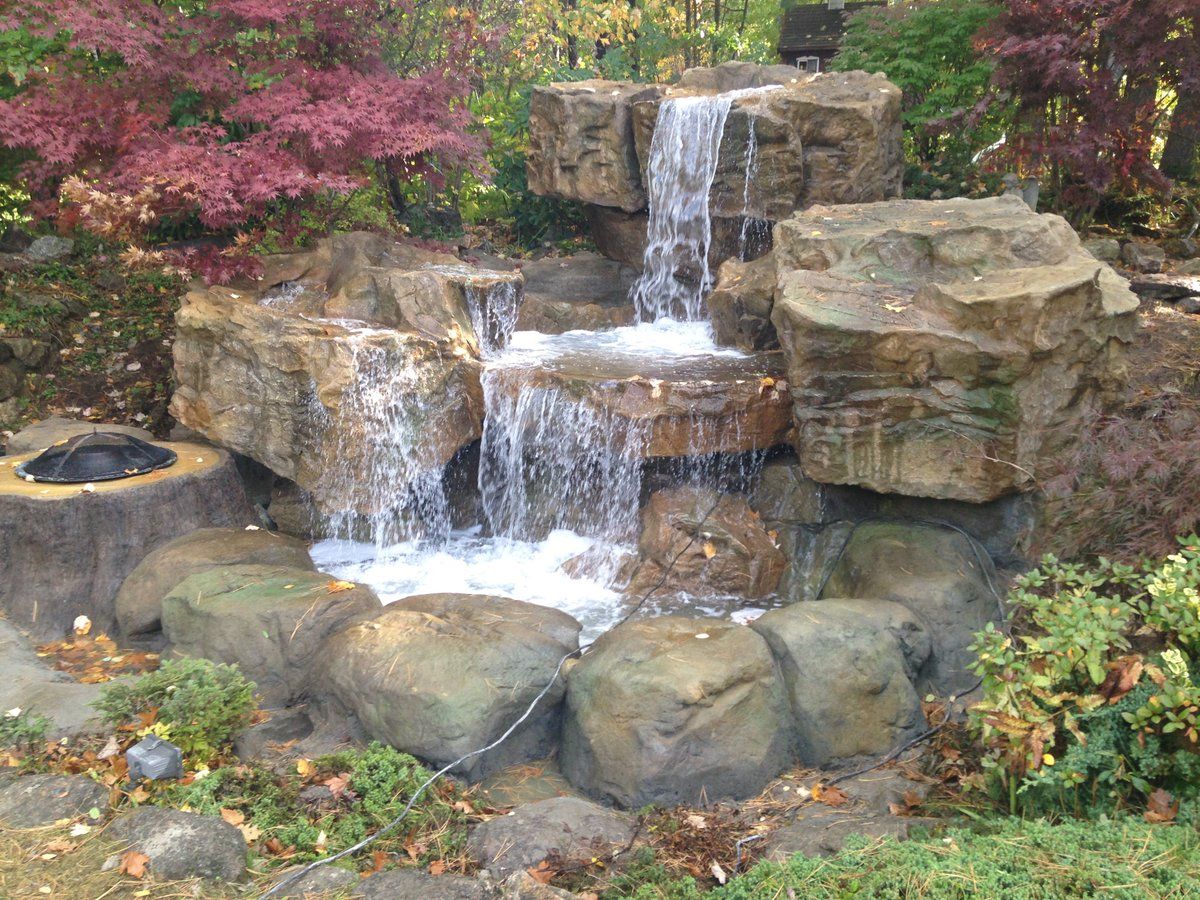 A waterfall is surrounded by rocks and trees in a garden.