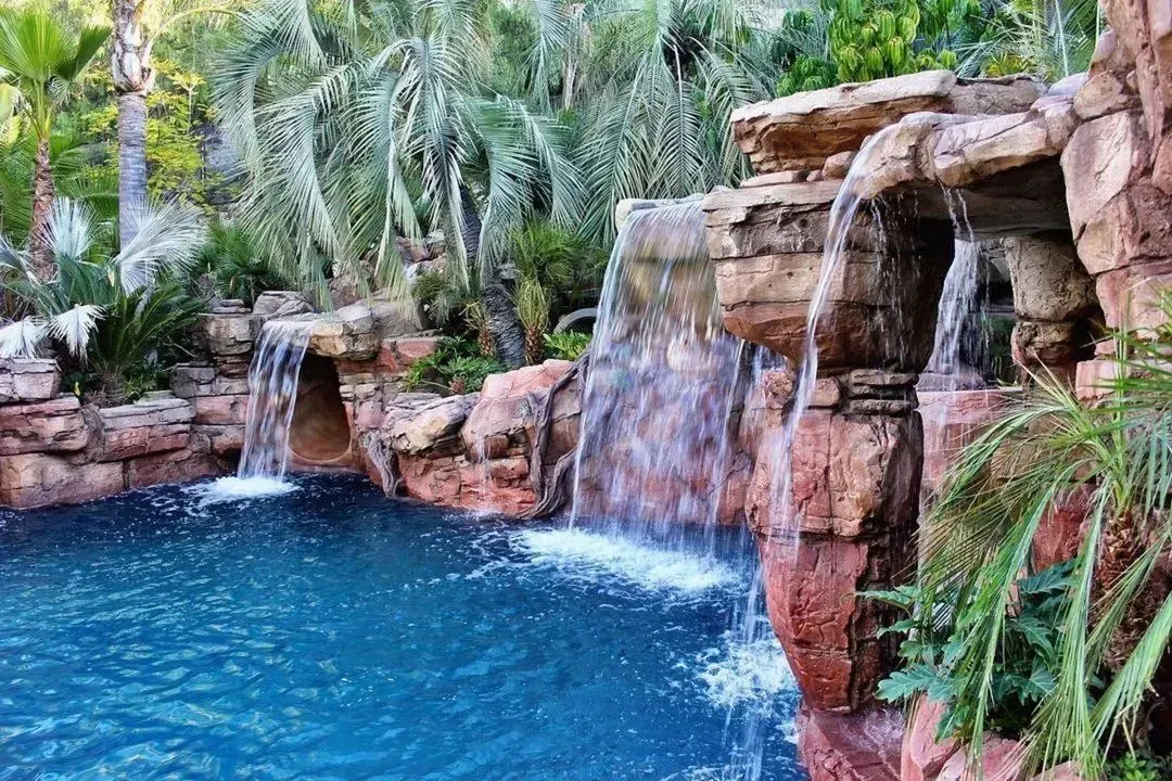 A swimming pool with a waterfall and chairs under a pergola. Waterfall builders in florida