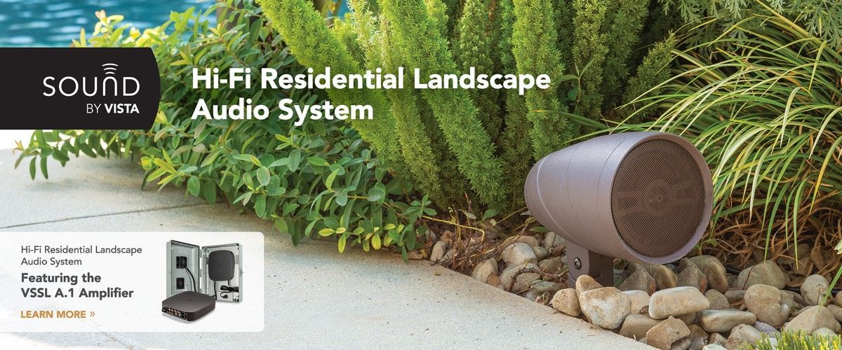 A speaker is sitting on a sidewalk next to a bush.