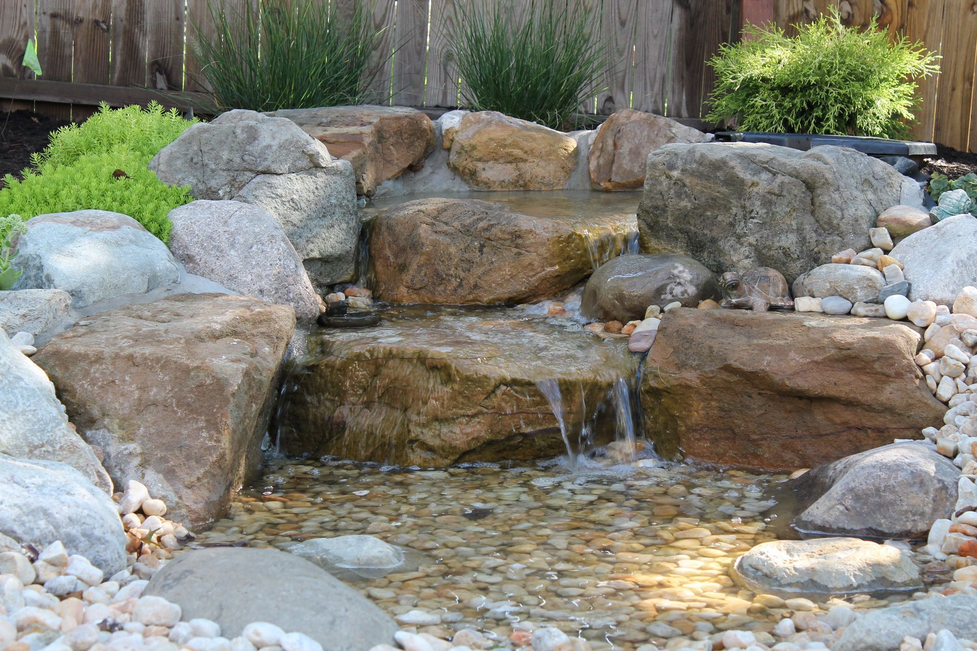 A small waterfall surrounded by rocks and gravel in a backyard.