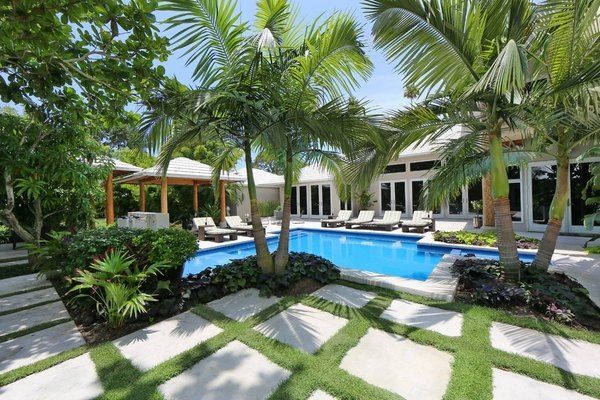 There is a large swimming pool in the backyard of a house surrounded by palm trees.