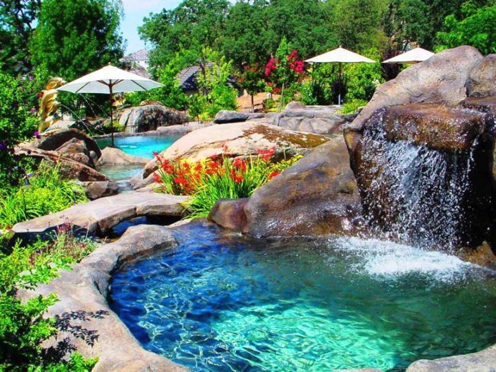 A swimming pool with a waterfall and umbrellas in the background