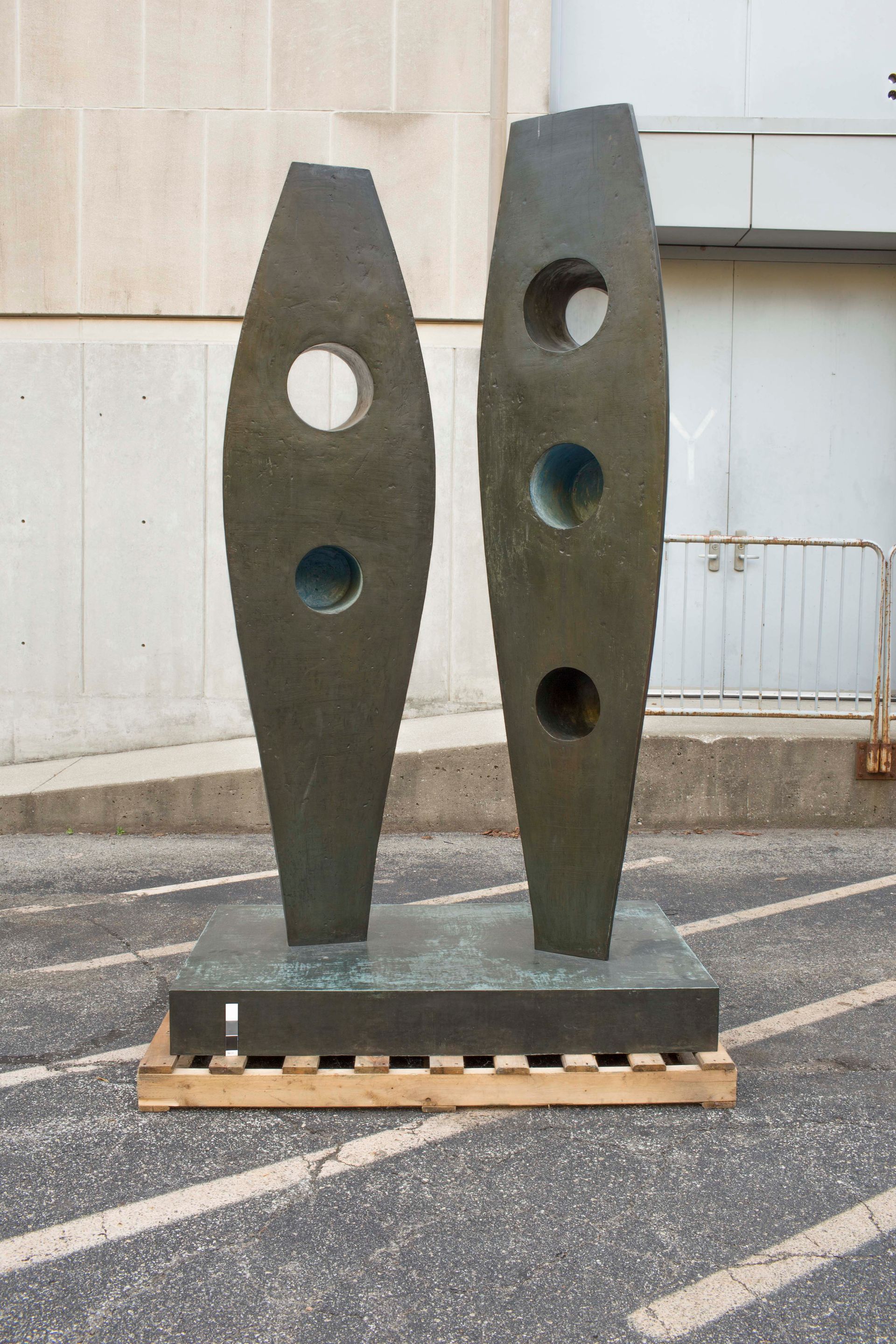 A tall, dark bronze sculpture with two abstract vertical forms, each containing multiple circular cutouts, on a pedestal.