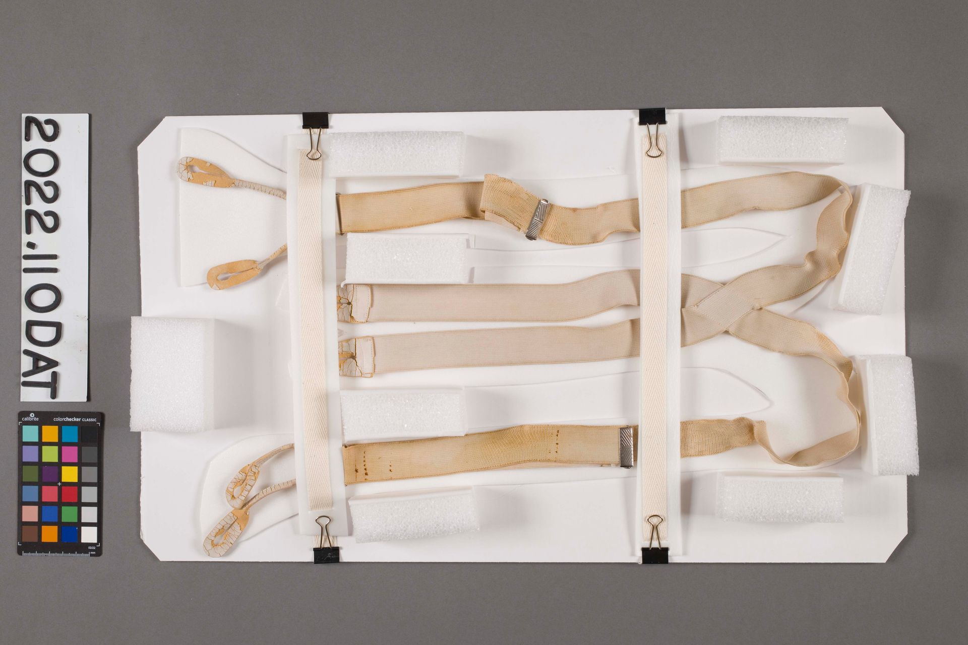 A display board featuring several tan fabric straps and foam padding blocks, accompanied by a color reference card.