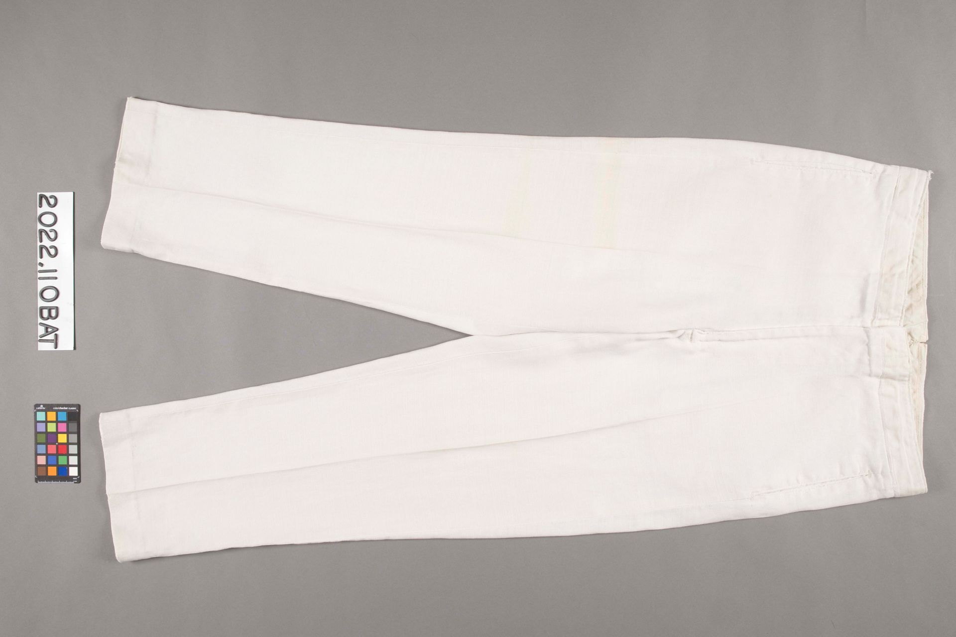 A pair of off-white trousers laid flat against a neutral gray background.