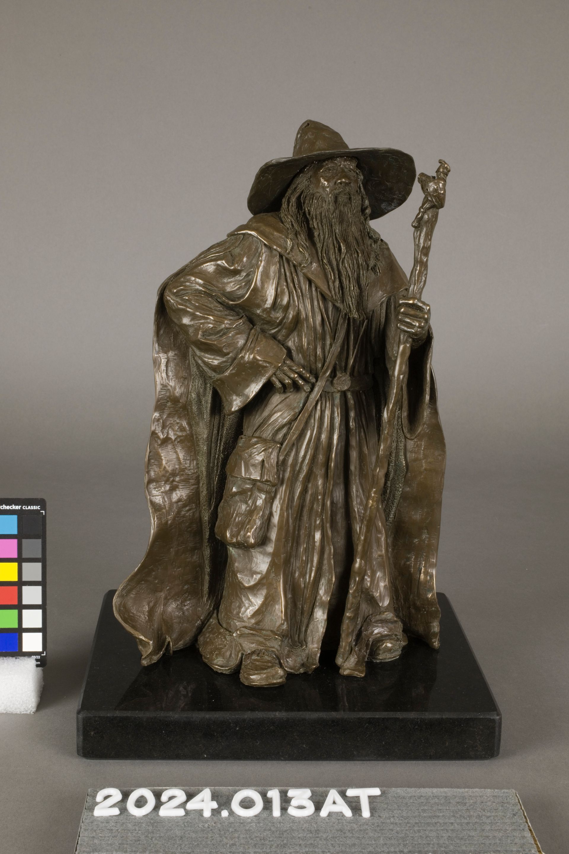 A bronze-toned sculpture of a bearded wizard in a wide-brimmed hat holding a staff, set on a black square base.