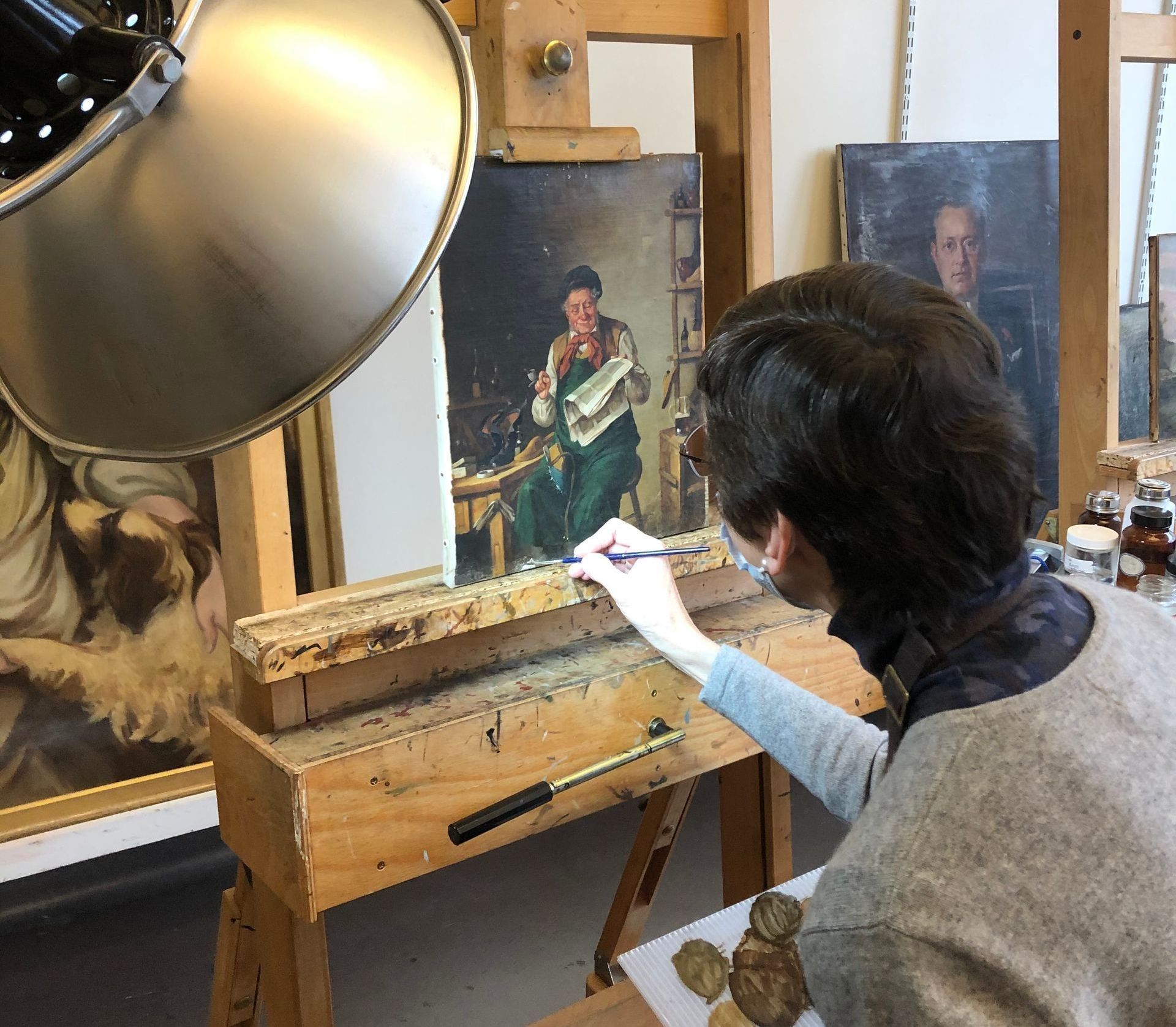 A man is painting a picture on an easel in a studio.