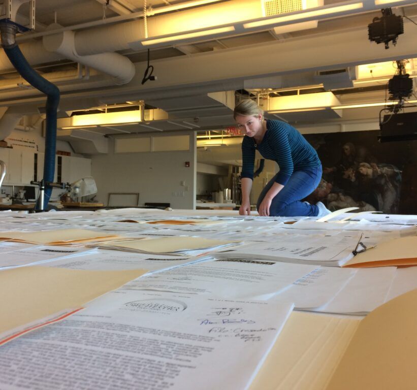 A woman is kneeling on a table with papers on it