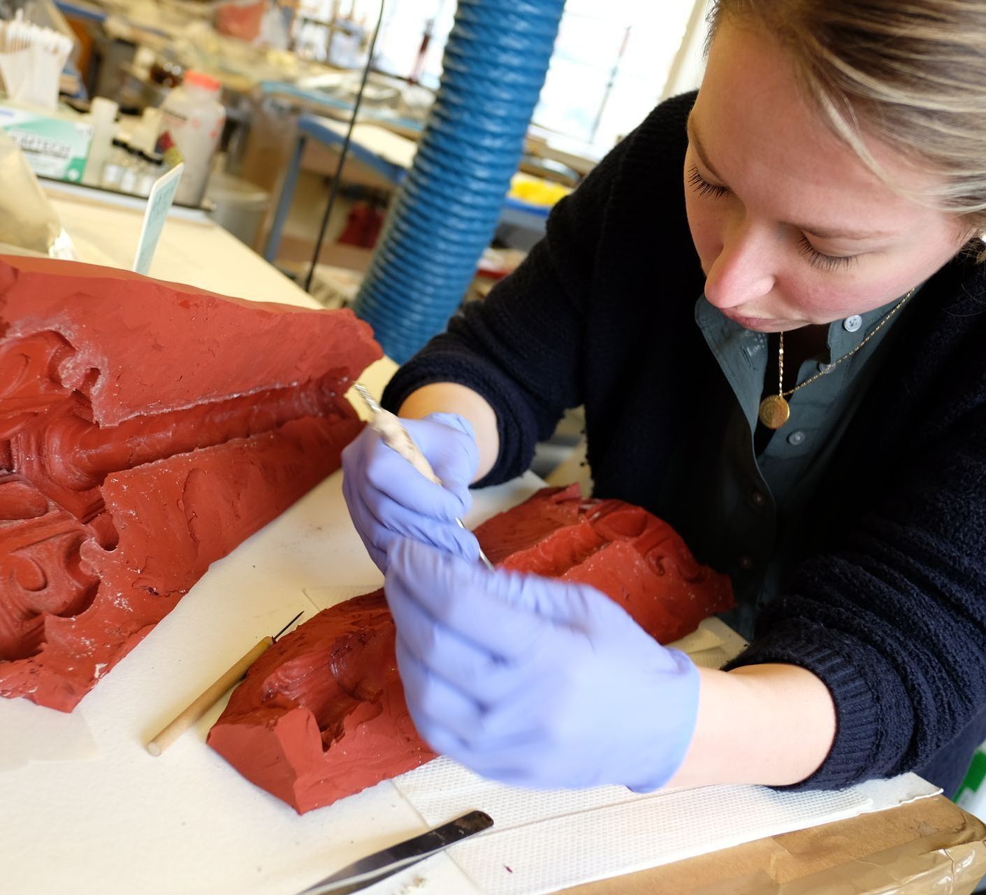 A woman wearing purple gloves is working on a red object