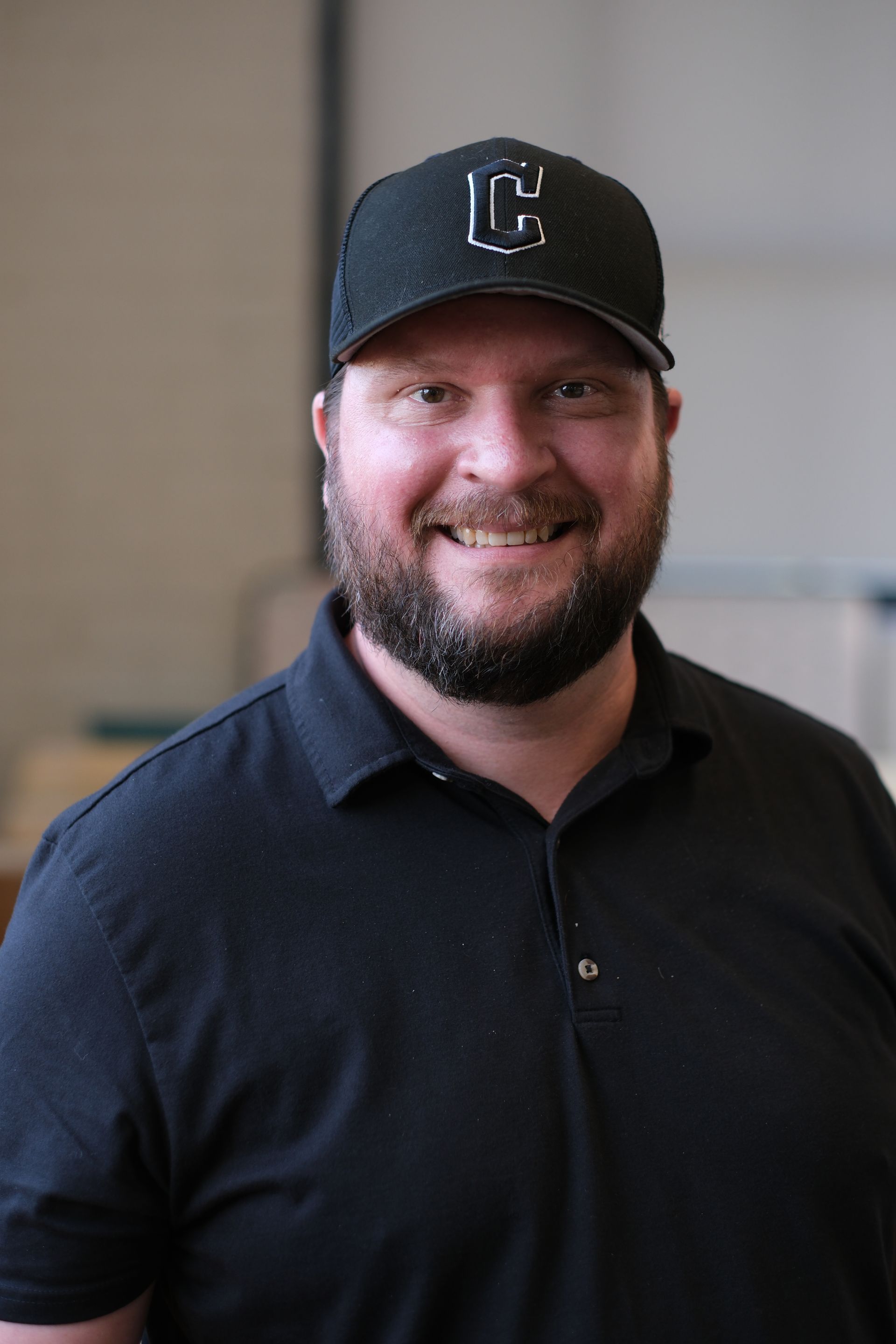 A man with a beard is wearing a black hat and smiling.