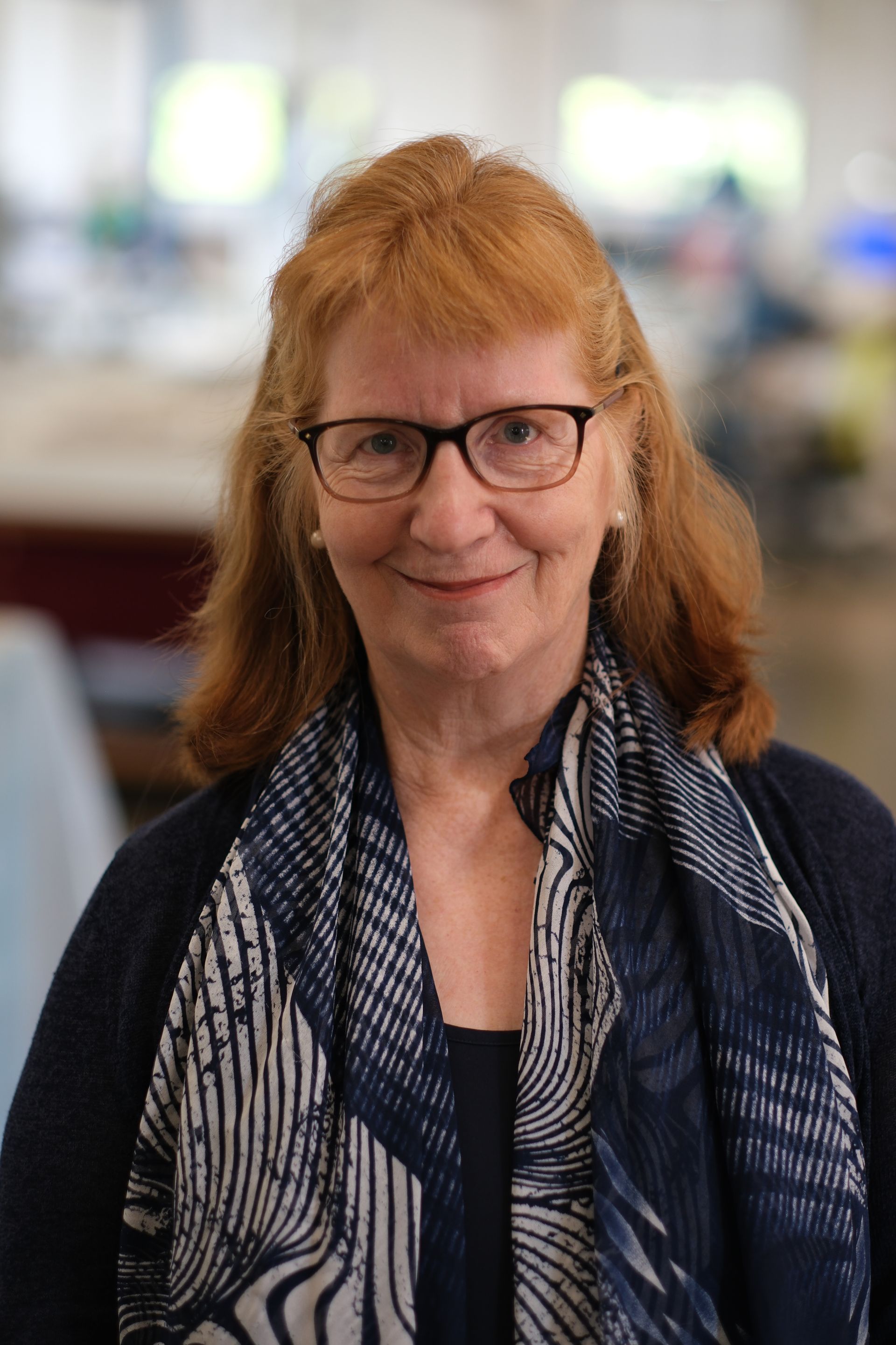 A woman wearing glasses and a scarf is smiling for the camera.