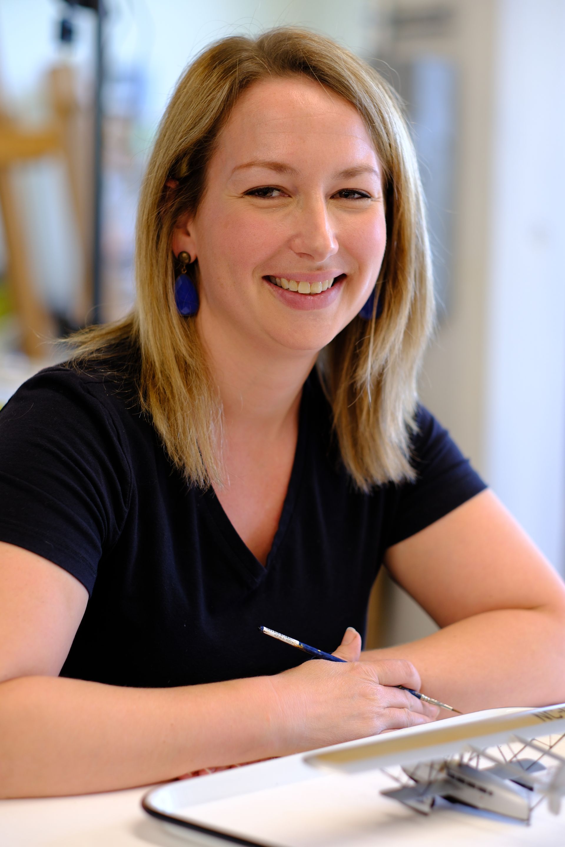 A woman is sitting at a table with a brush in her hand and smiling.