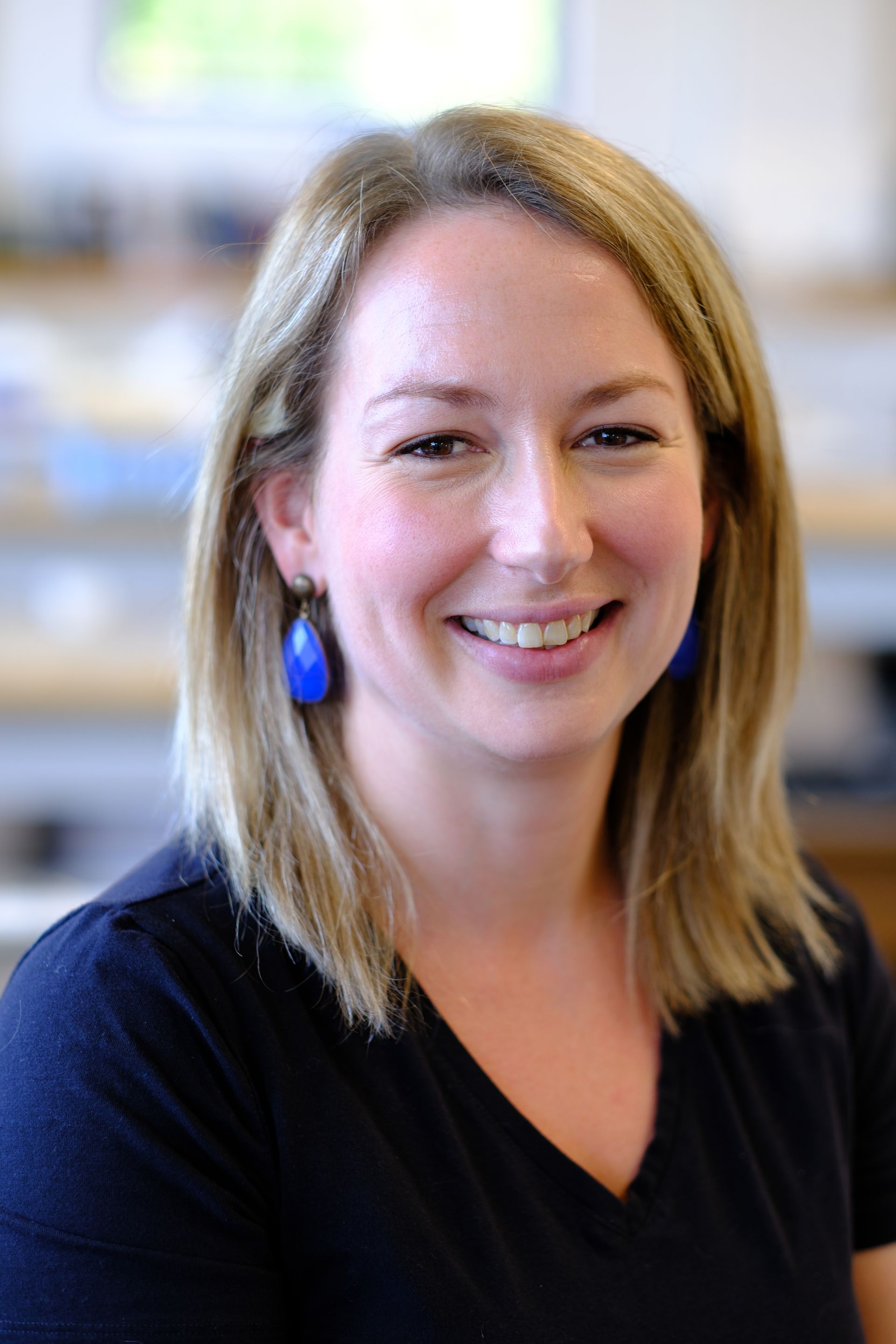 A woman wearing a black shirt and blue earrings is smiling for the camera.