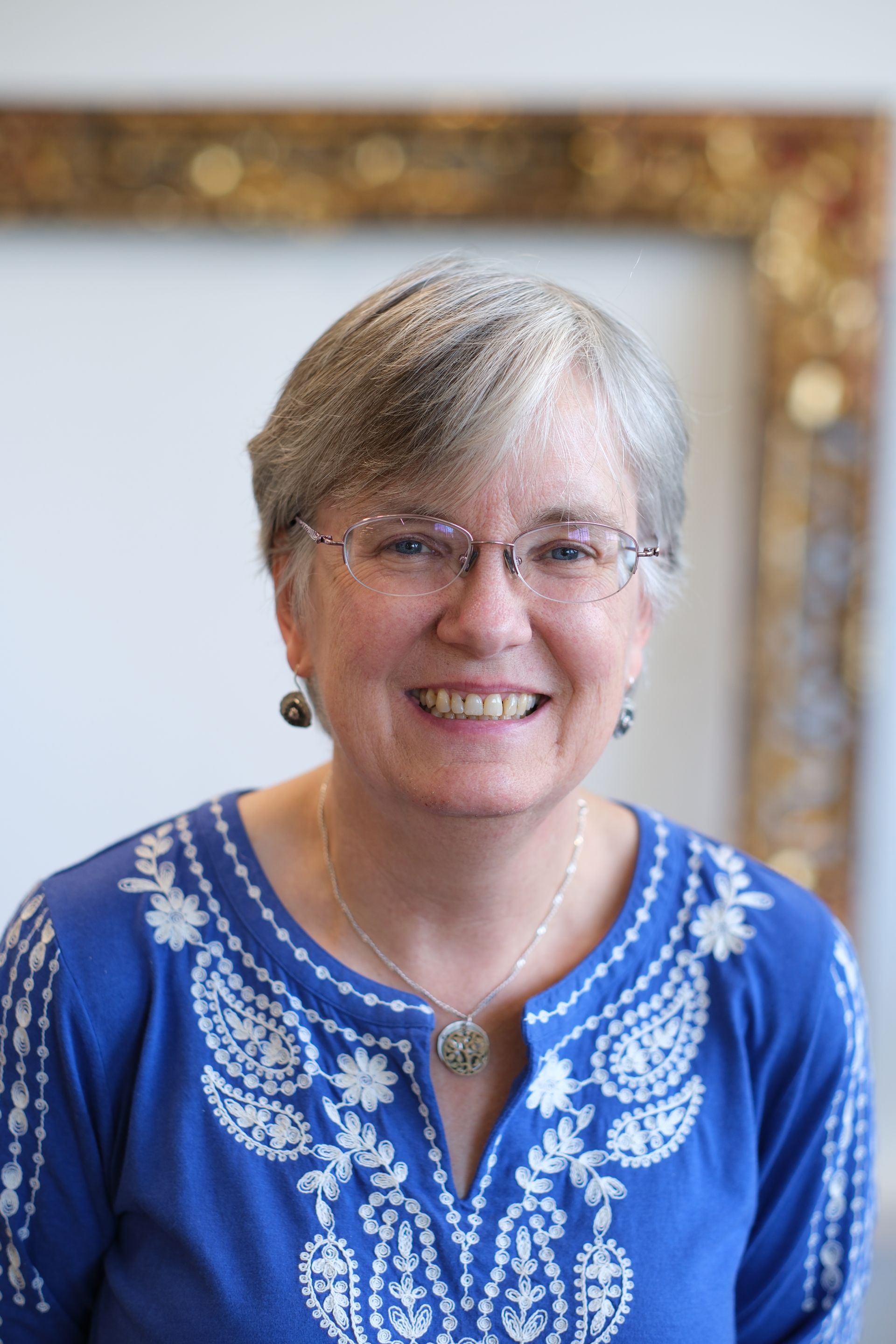 A woman wearing glasses and a blue shirt smiles for the camera