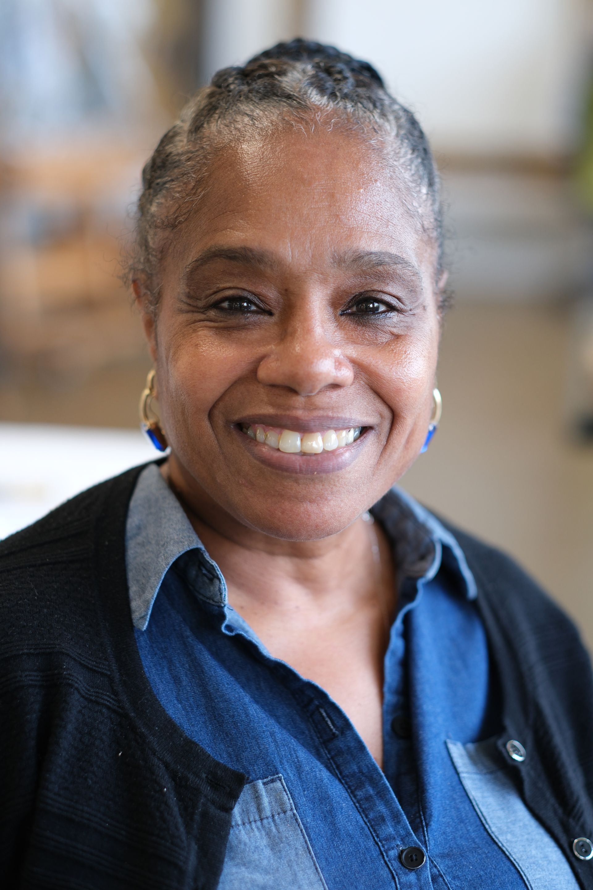 A woman in a pink jacket is smiling with her hand on her chin.