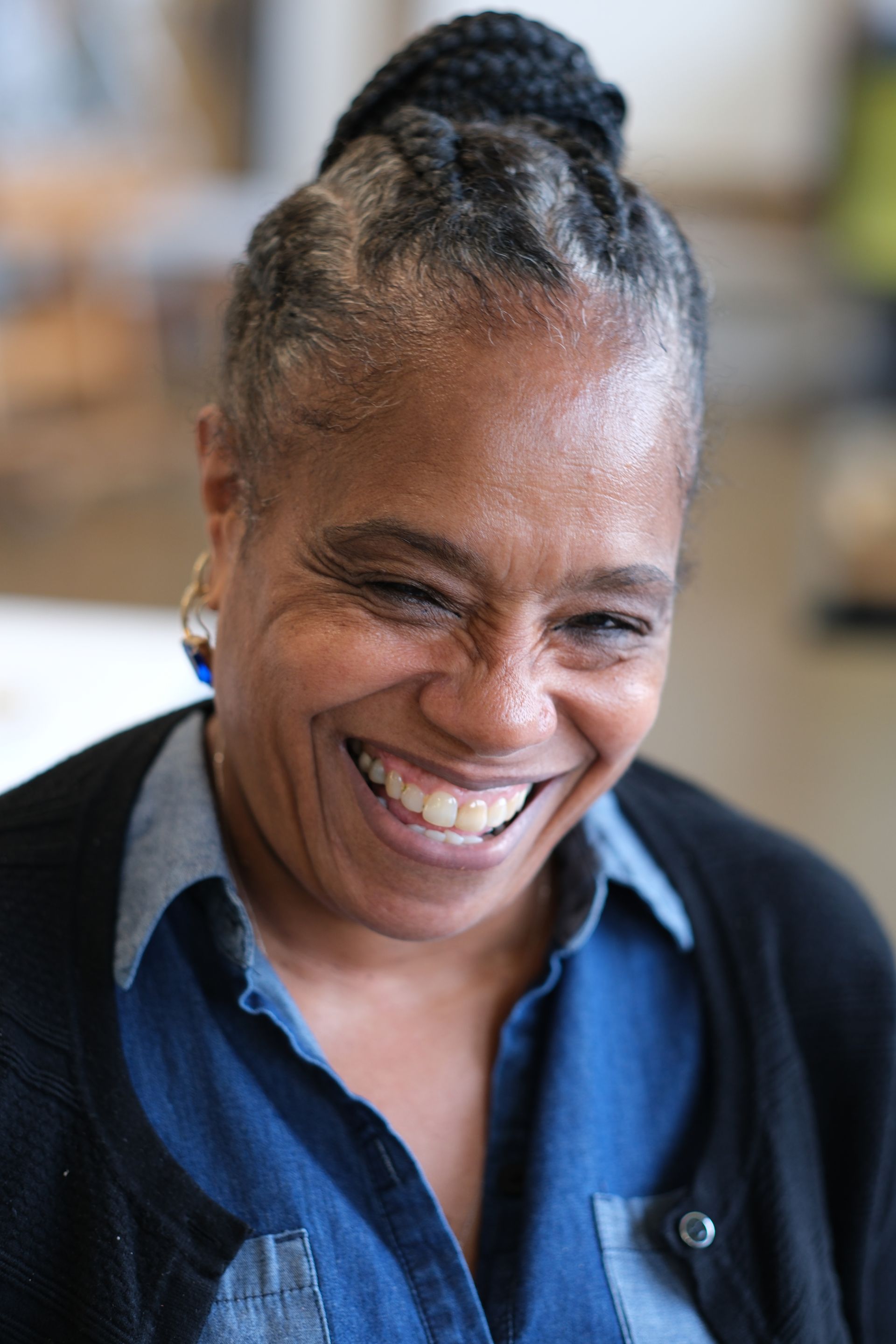 A woman is smiling and wearing a black sweater and a blue shirt.