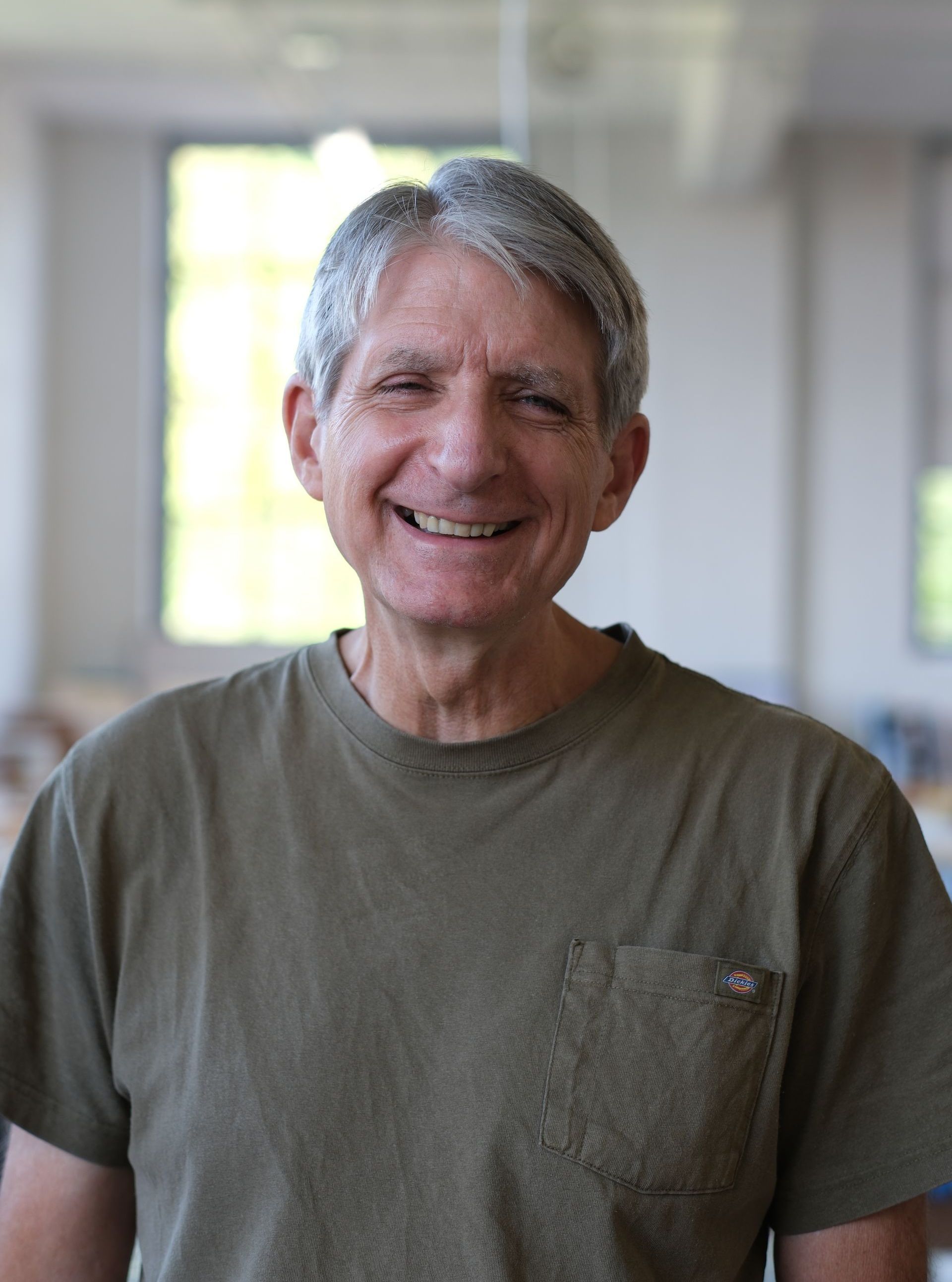 A man with gray hair is wearing a green shirt and looking at the camera.