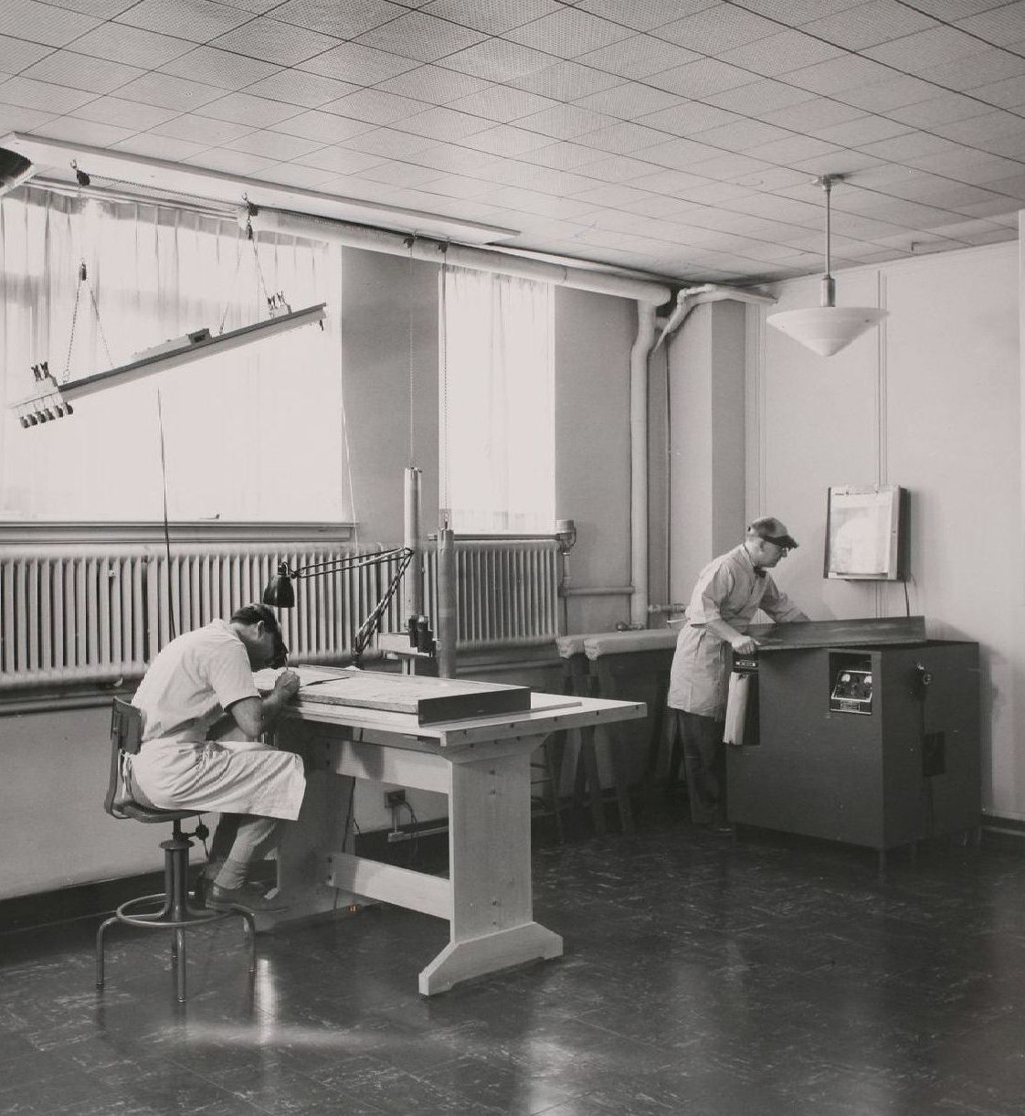 A black and white photo of two men working in a room