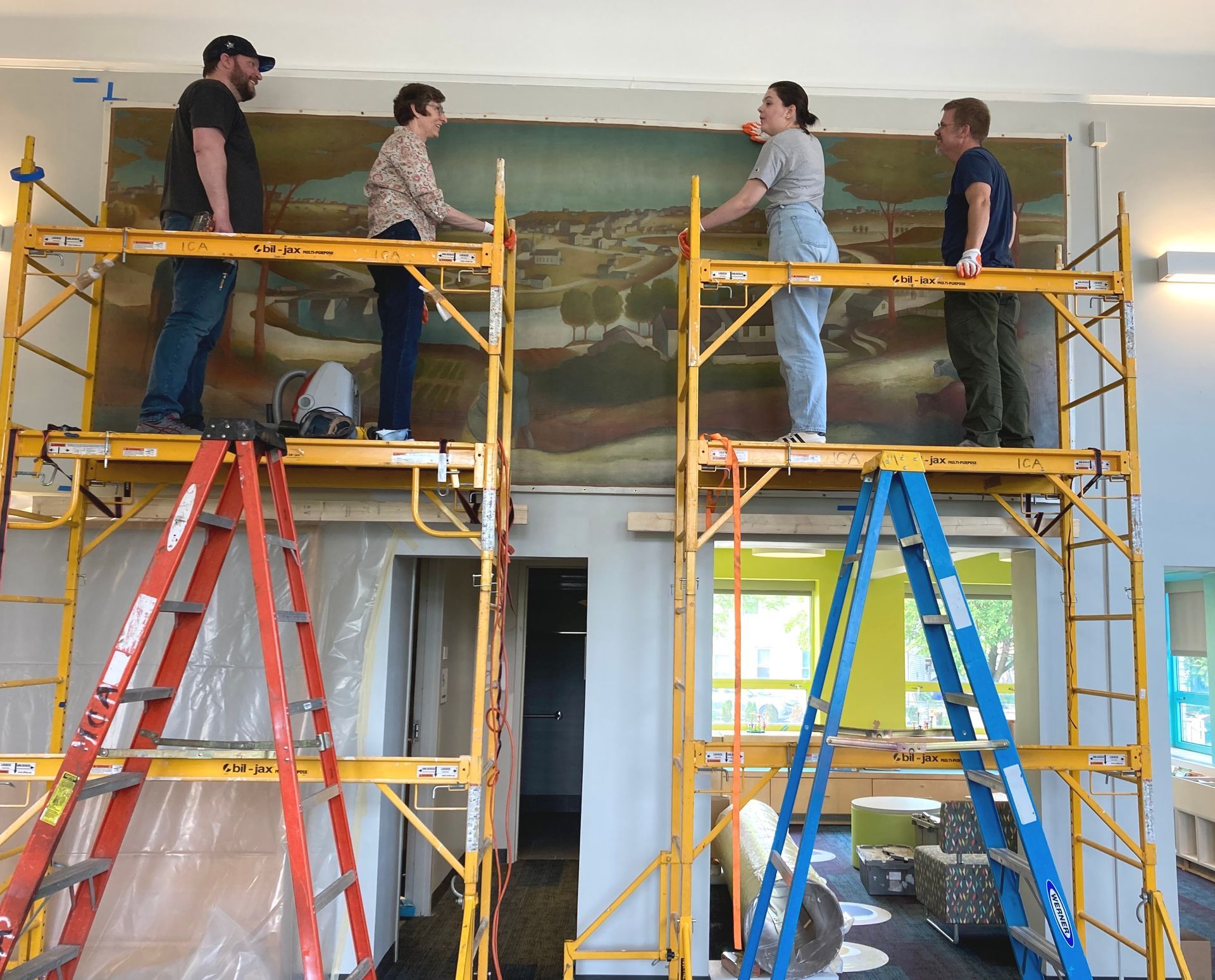 A group of people standing on scaffolding in front of a painting