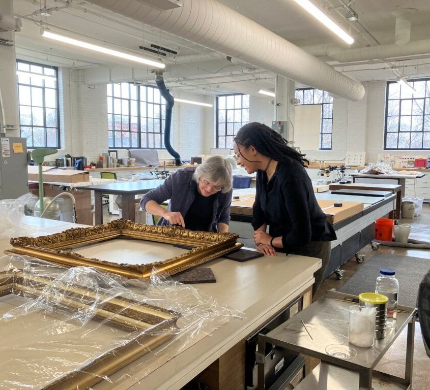 Two women are looking at a picture frame on a table.