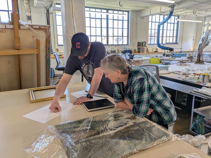 A man in a purple shirt is working on a painting on a table