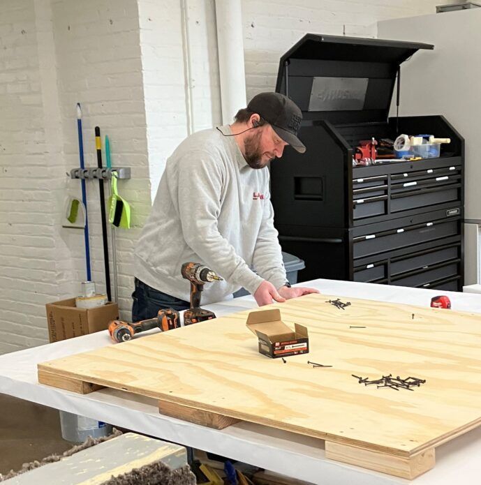 A man is working on a wooden pallet with a drill