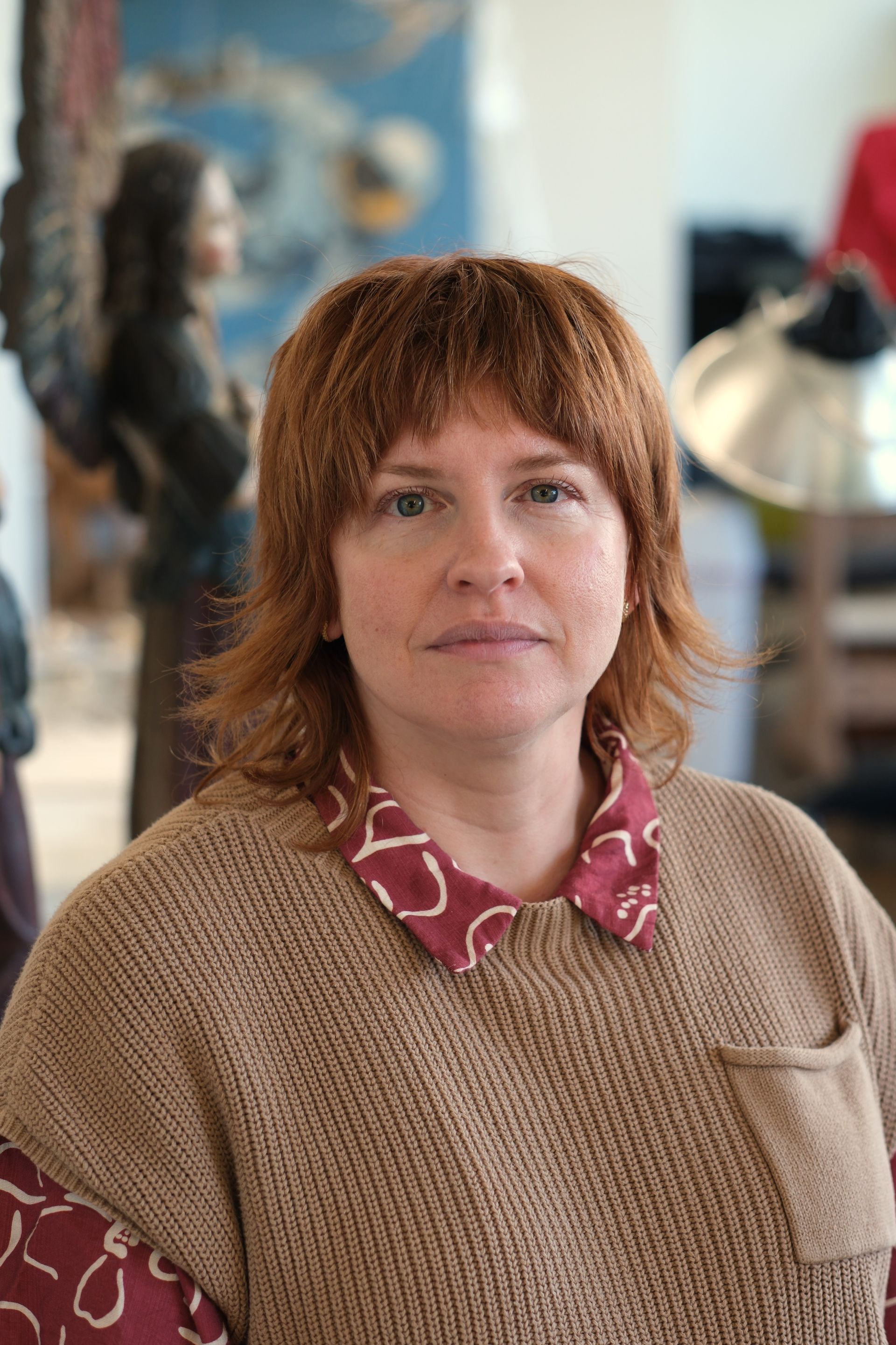 A woman wearing a denim shirt and a brooch is smiling for the camera.