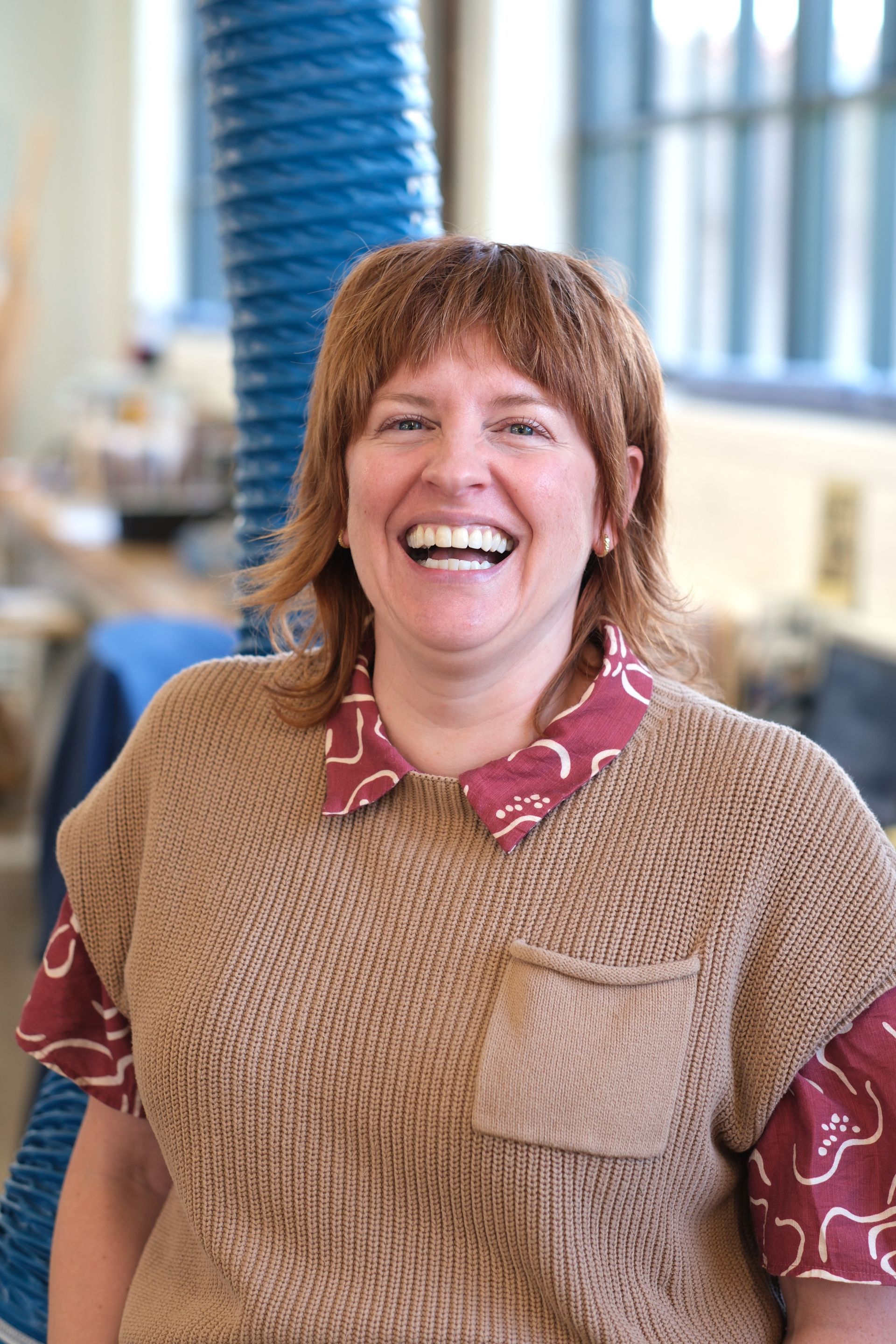 A woman is smiling with her eyes closed and wearing a denim shirt.