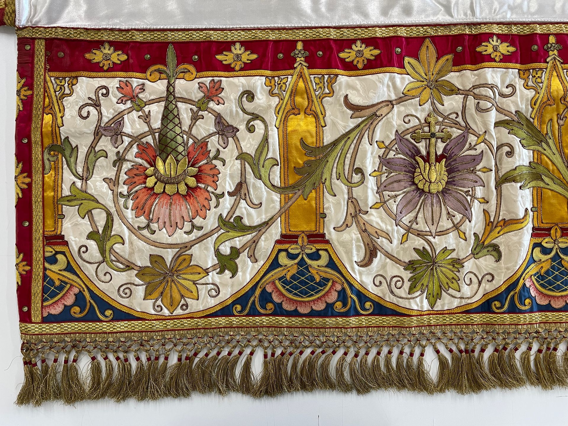 Ornate textile with cream satin, red velvet, and gold embroidery featuring floral motifs and a golden fringe border.