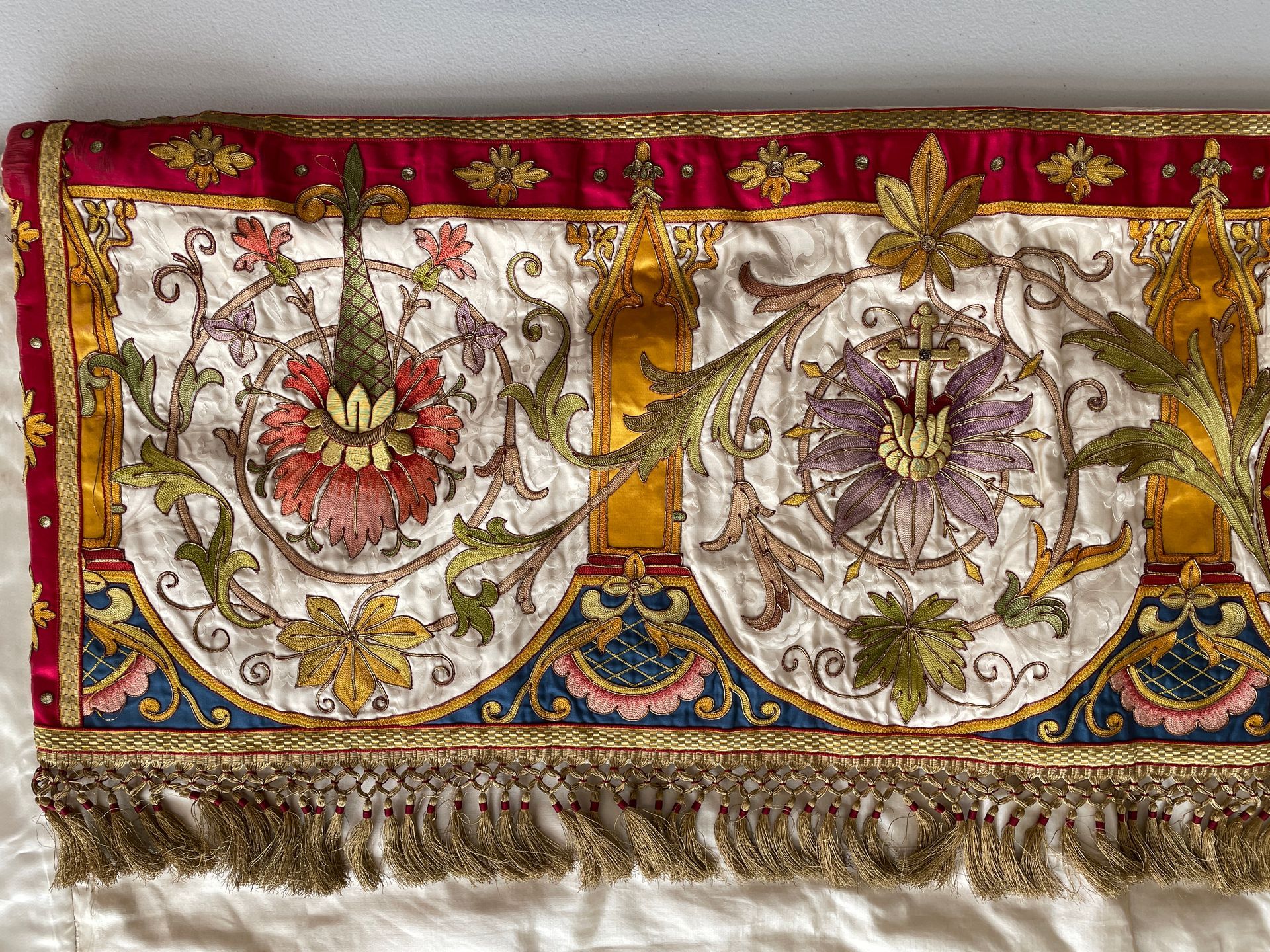 Ornate textile border featuring gold, red, and cream silk embroidery with floral patterns and a metallic fringe edge.