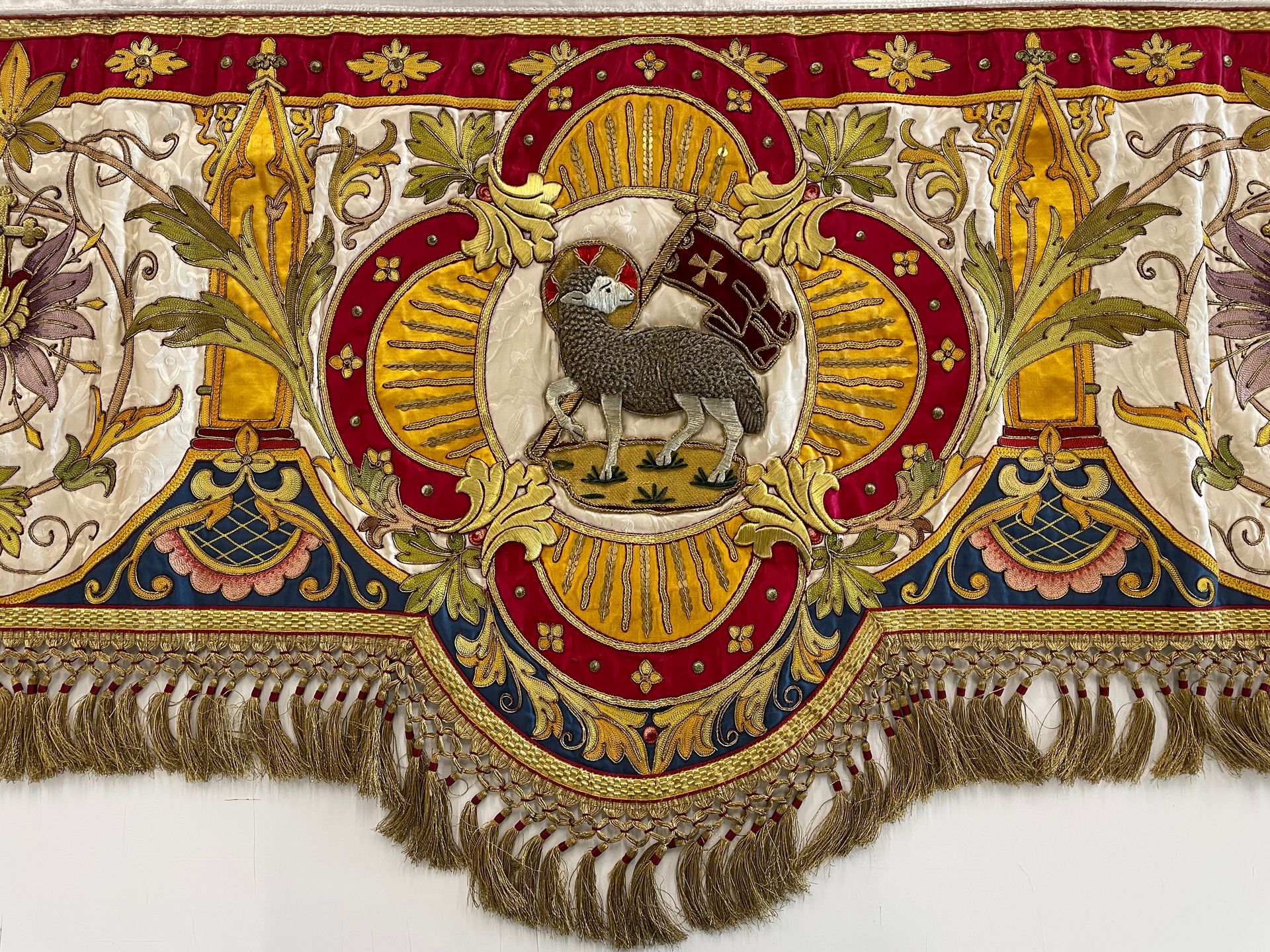 Ornate velvet textile featuring a central Agnus Dei lamb with a cross flag, surrounded by gold embroidery and tassels.