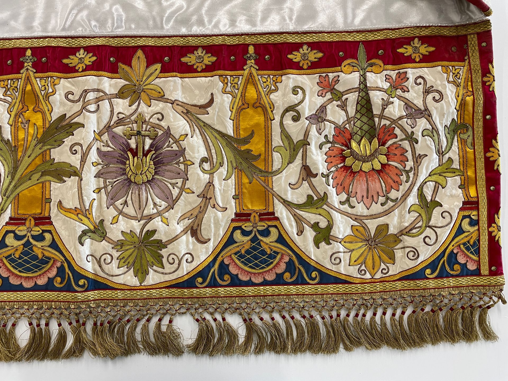 A close-up of decorative, ornate ecclesiastical embroidery featuring floral motifs, metallic gold trim, and fringe.