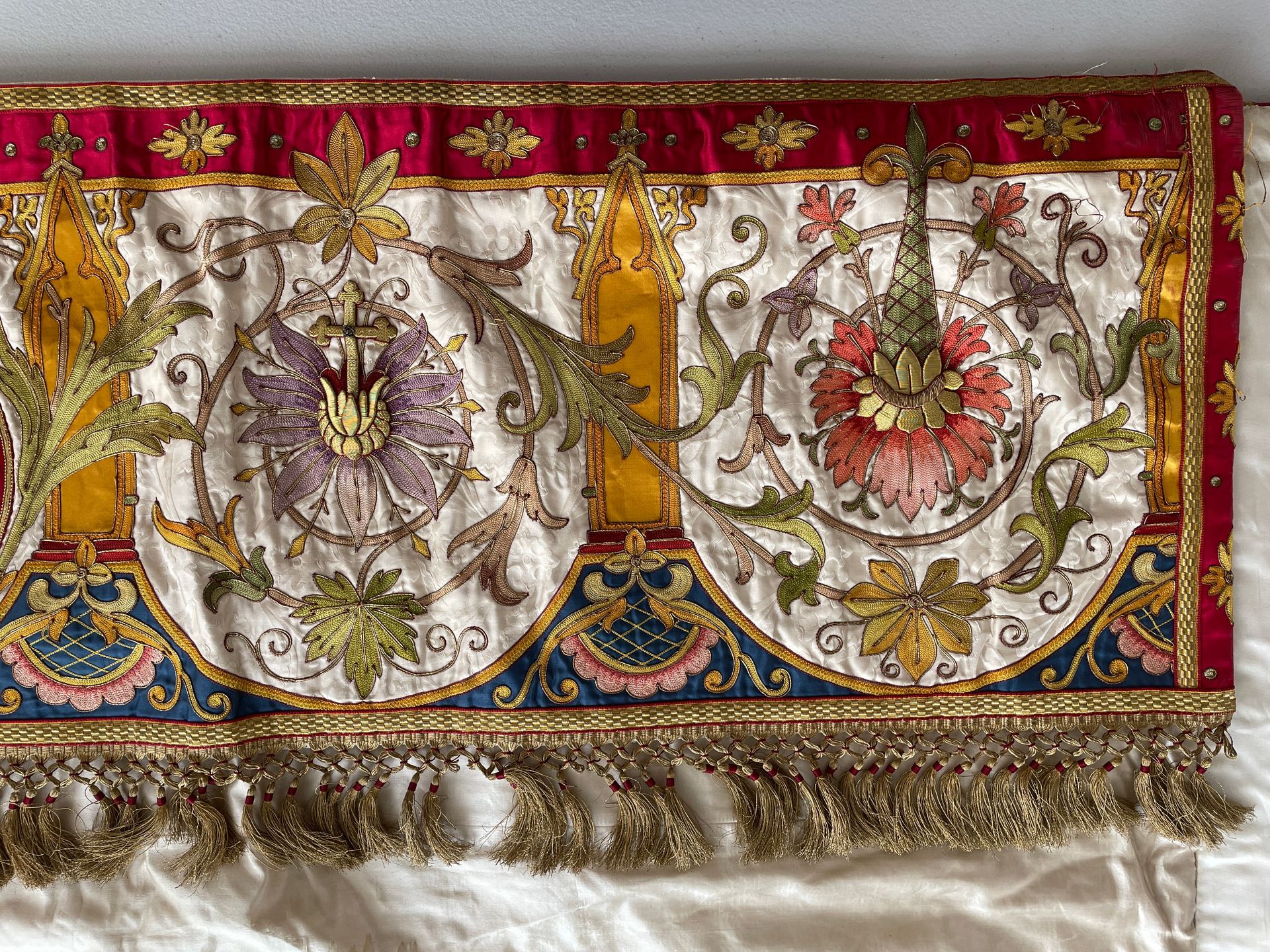 A rectangular fabric border with gold embroidery, floral motifs, and fringe on a white, red, and blue background.