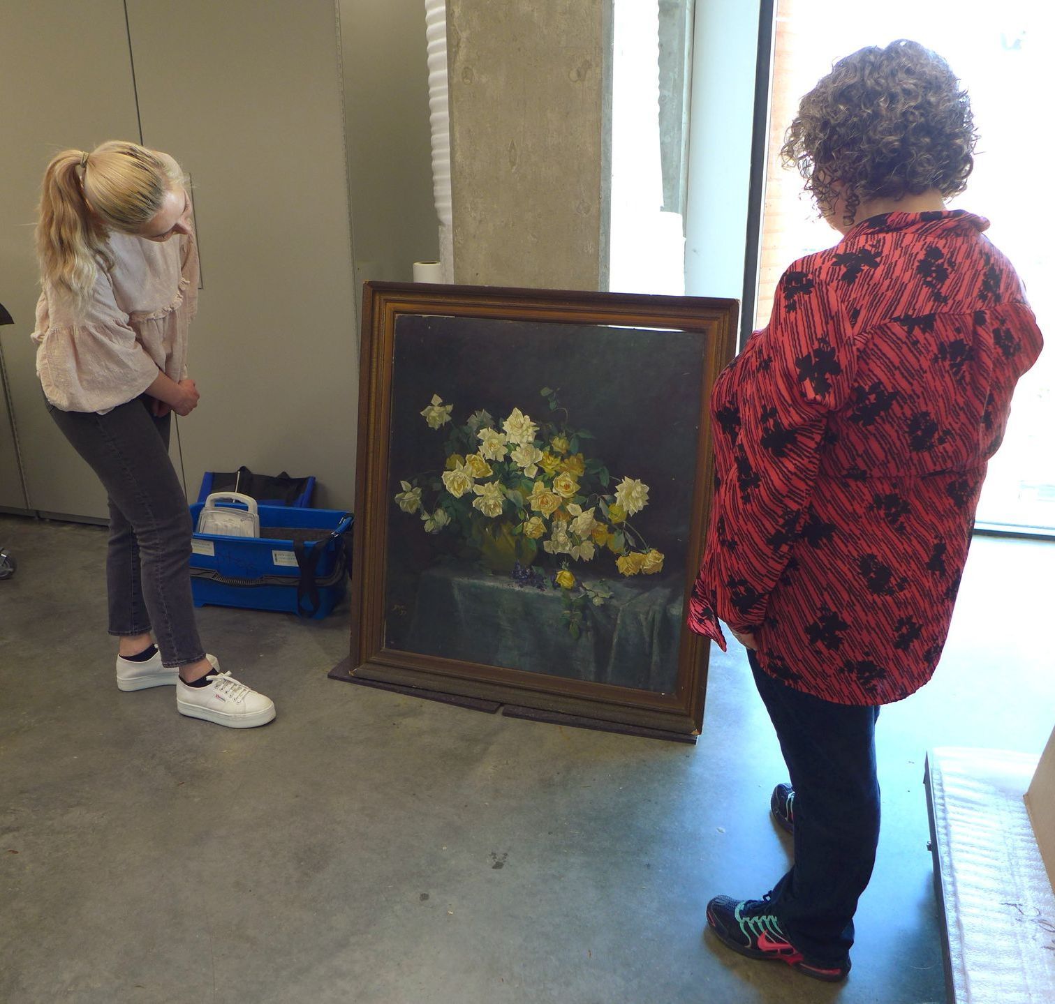 Two women are looking at a painting of flowers in a vase