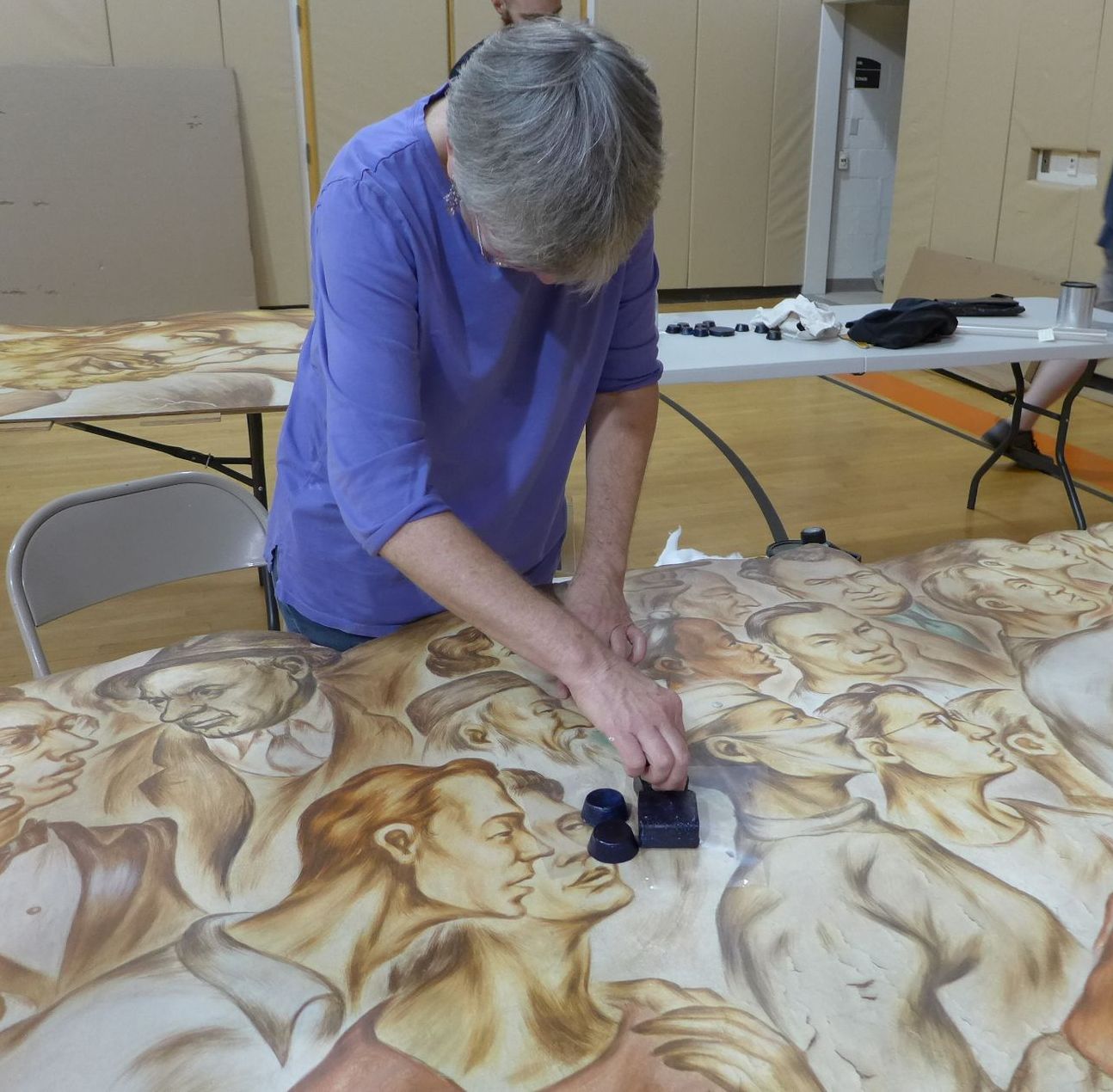 A man in a purple shirt is working on a painting on a table