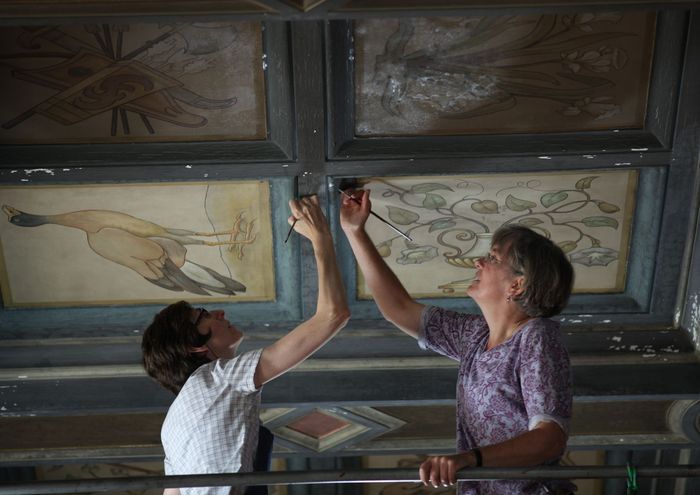 Two women are looking at a painting on the ceiling.