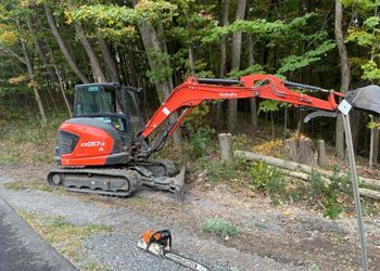 A red excavator is parked on the side of the road next to a chainsaw.