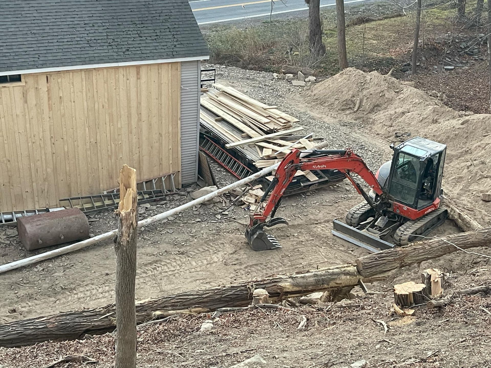 A small red excavator is sitting in the dirt in front of a shed.