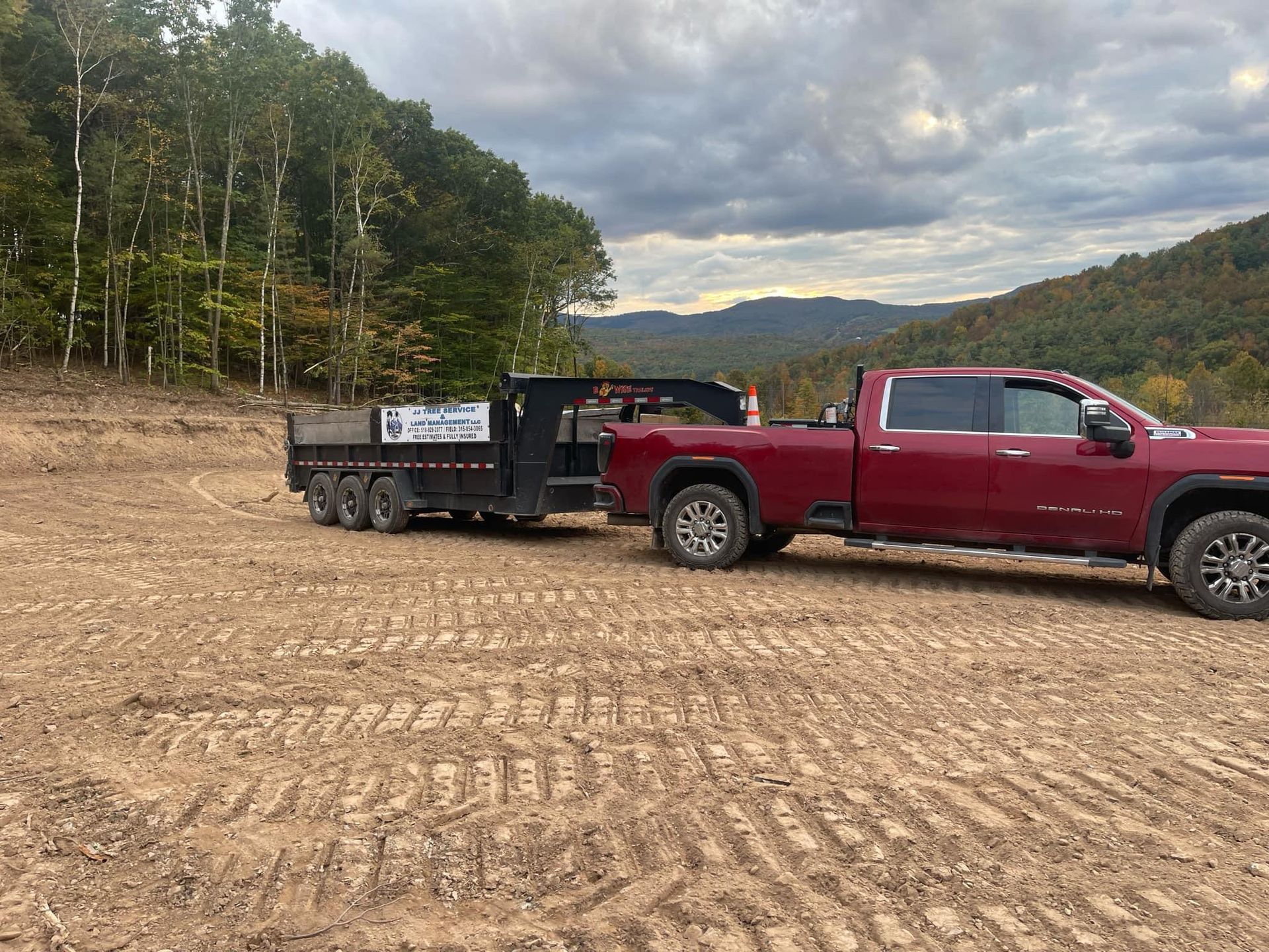 A red truck is towing a trailer in a dirt field.
