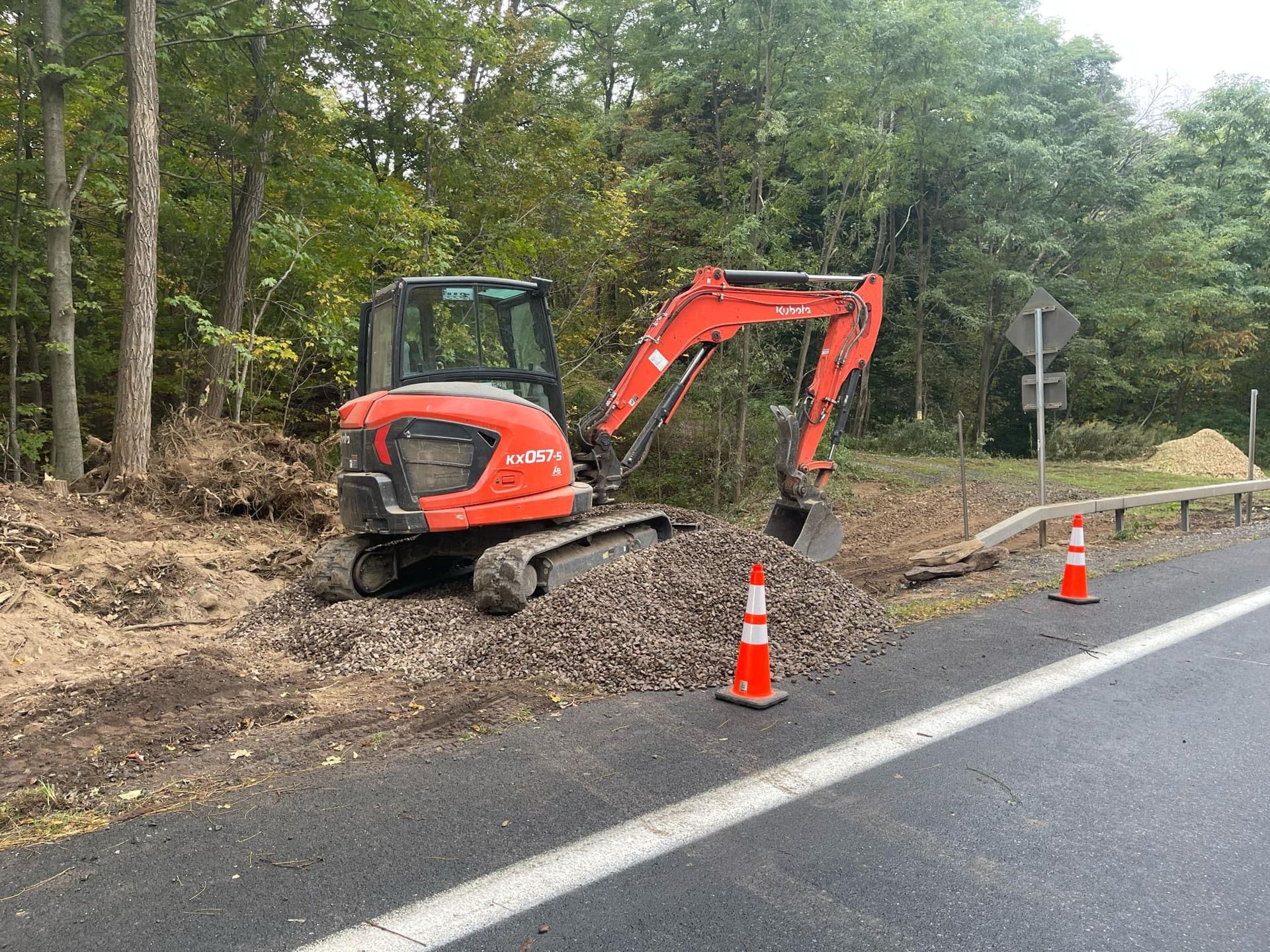 A red excavator is digging a hole on the side of a road