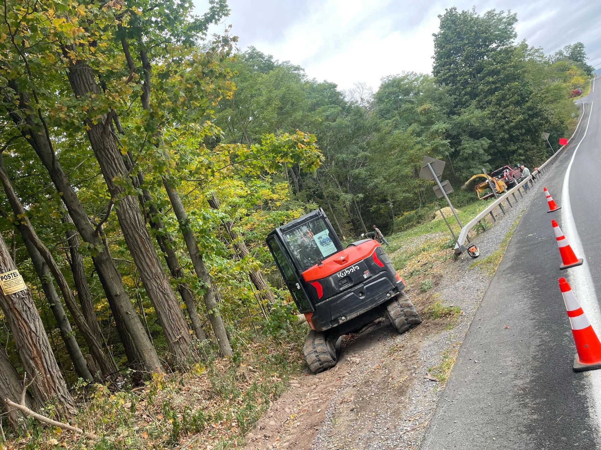 A red and black excavator is sitting on the side of a road.
