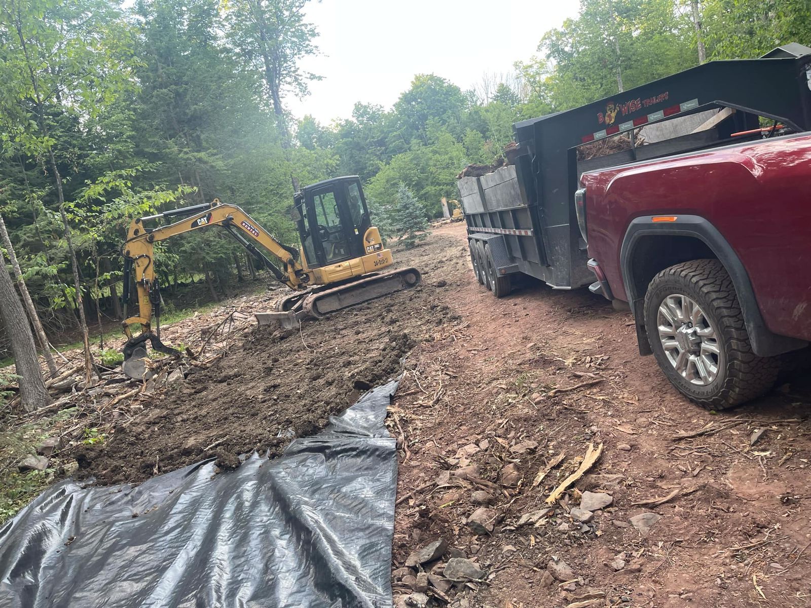 A red truck is parked next to a bulldozer on a dirt road.