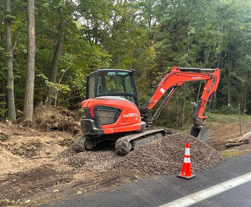 A red excavator is sitting on a pile of dirt next to a road.