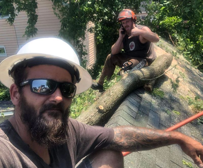 A man wearing a hard hat is sitting on a roof next to another man