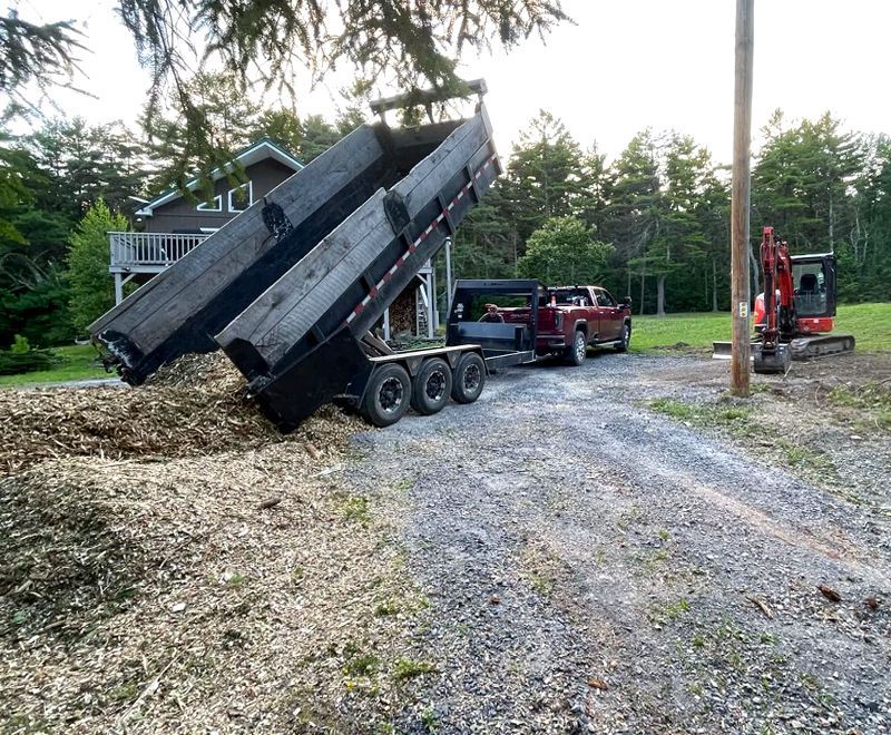 A dump truck is sitting on a gravel road next to a house.