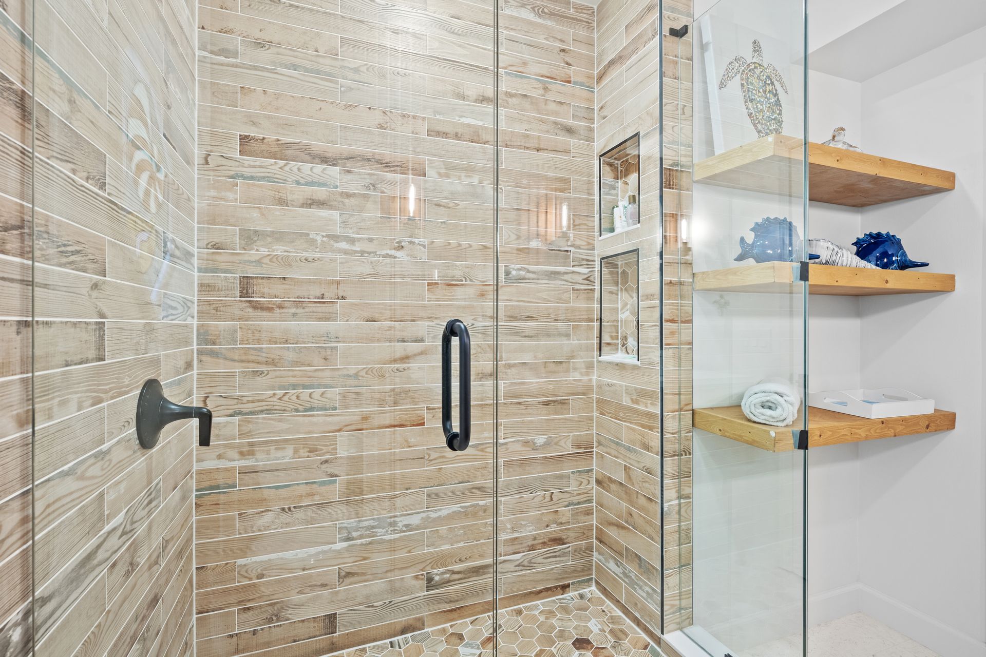 A bathroom with a walk in shower with a glass door and wooden shelves.